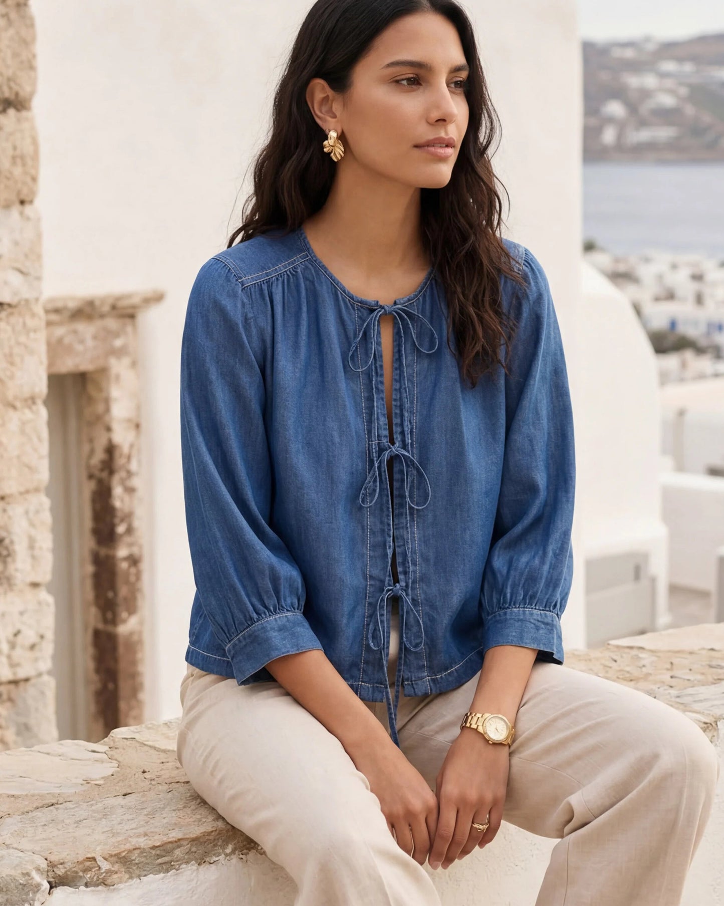 Model wearing chambray lantern sleeve top sitting on a wall with a scenic background