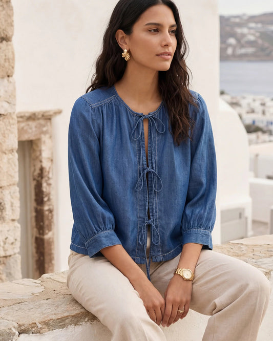 Model wearing chambray lantern sleeve top sitting on a wall with a scenic background