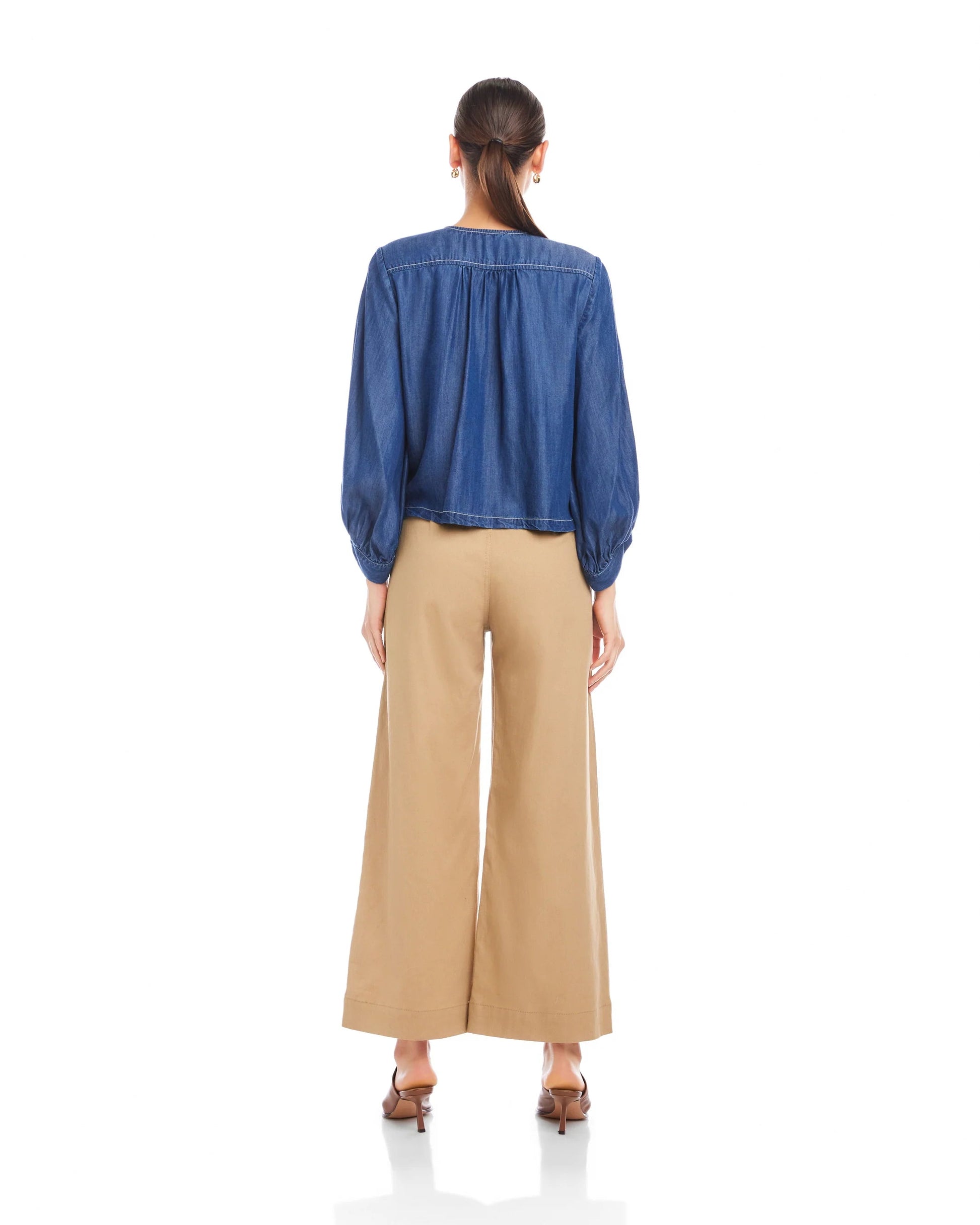 Back view of lantern sleeve top with tan pants on a model in front of a white background