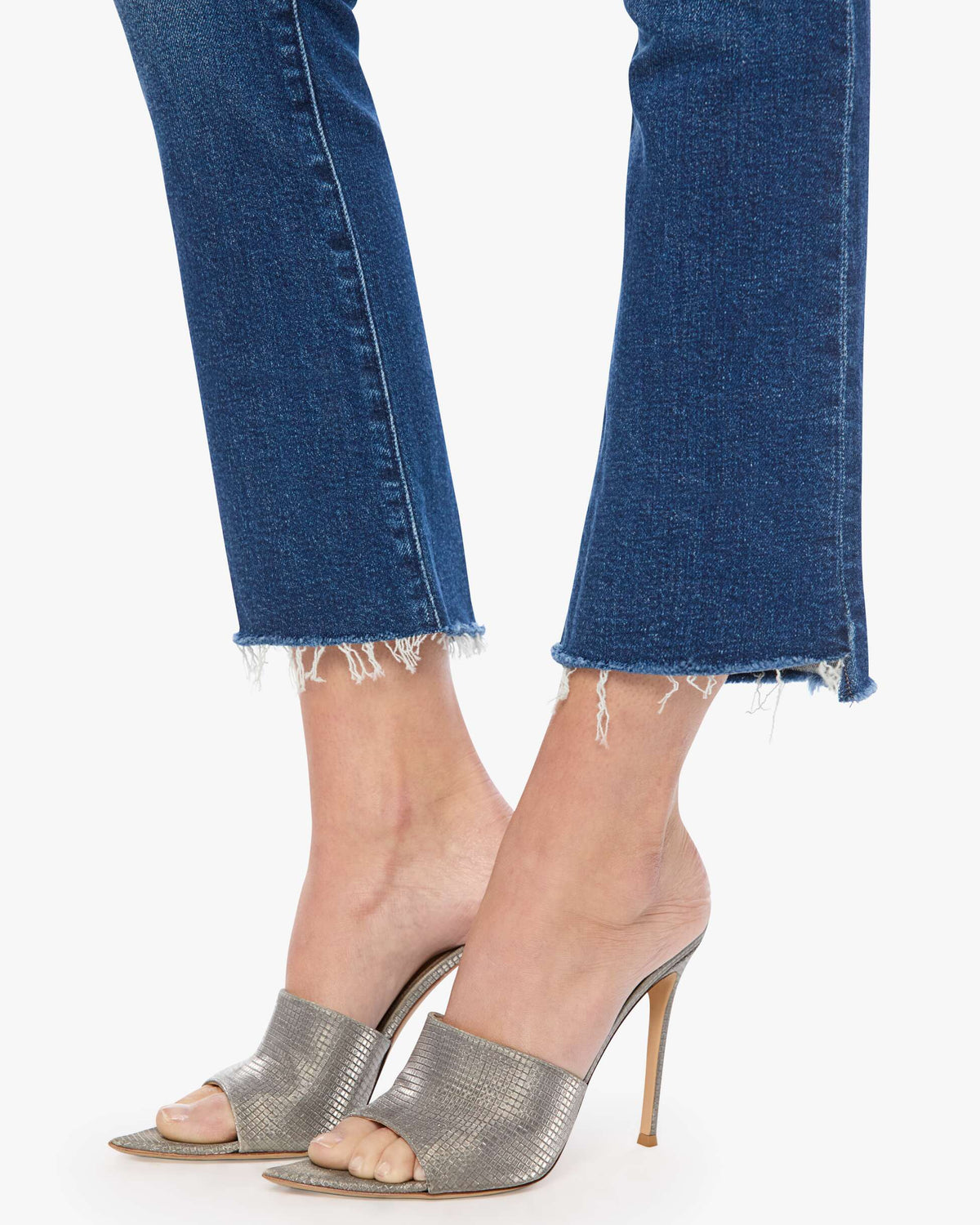 Close-up of legs wearing blue jeans and silver high-heeled shoes on a white background
