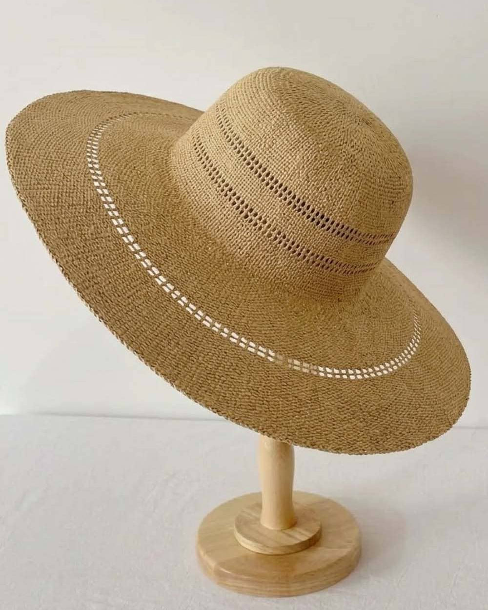 Brown straw hat with decorative band on a wooden stand against a white background