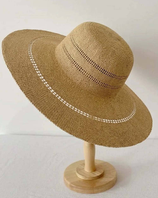 Brown straw hat with decorative band on a wooden stand against a white background