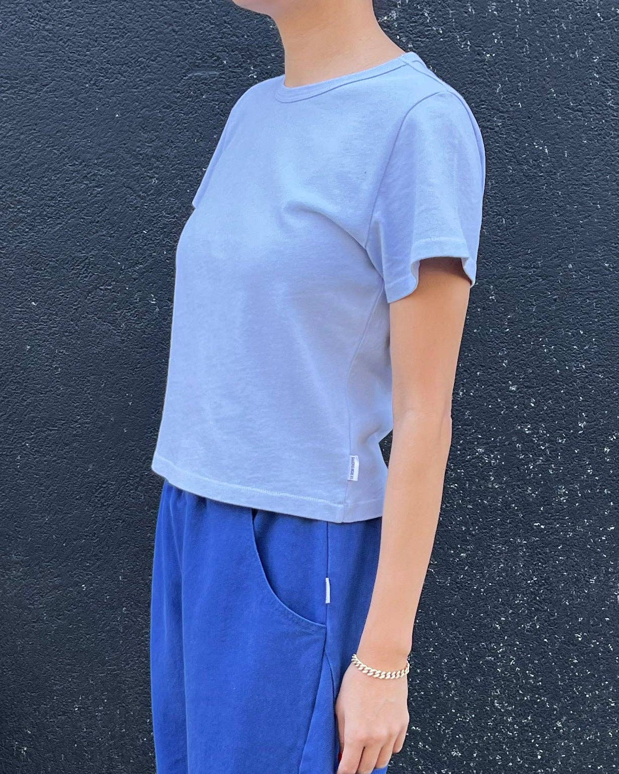 Person wearing a light blue t-shirt and blue pants against a dark textured wall.