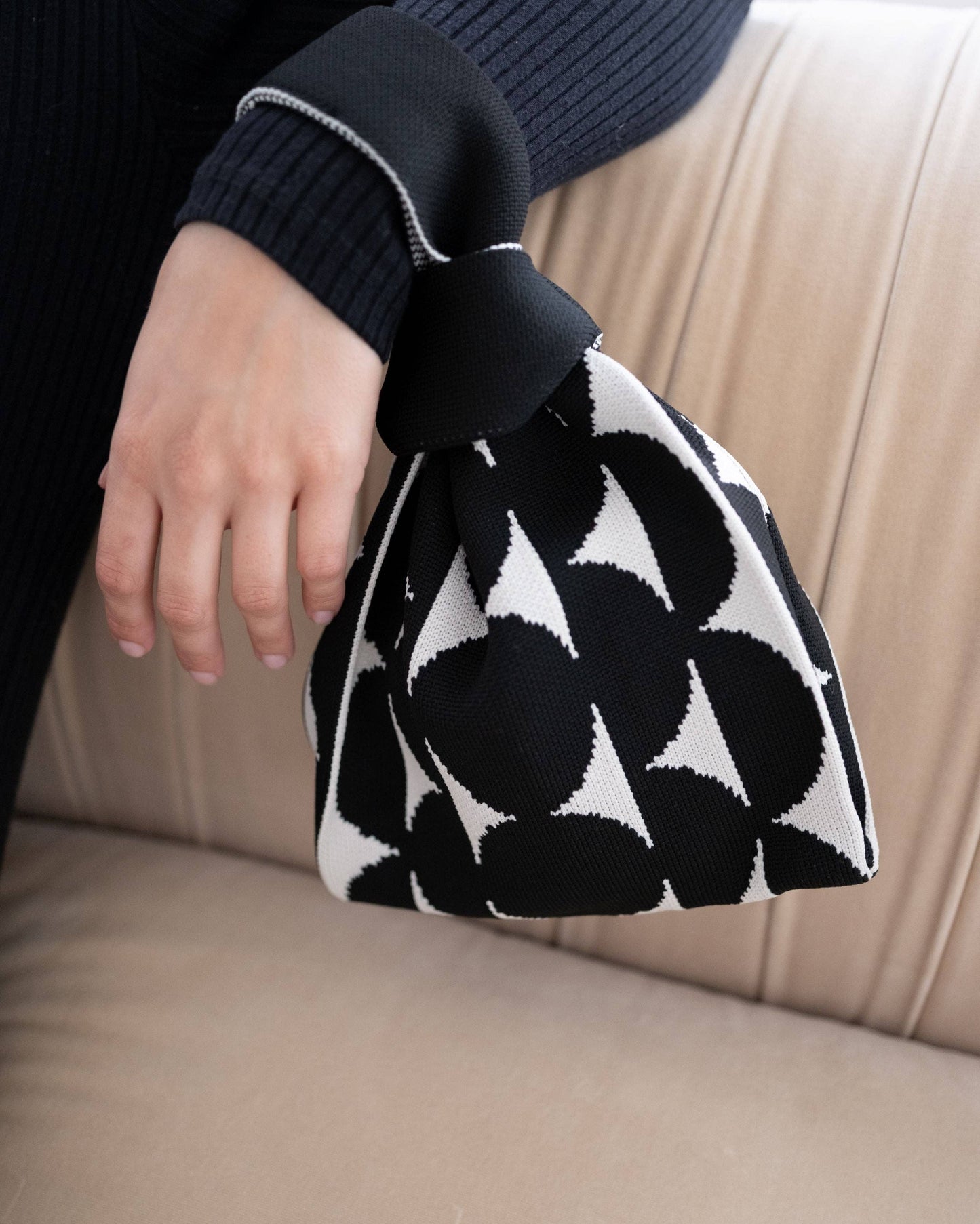 Person holding a black and white patterned bag on a beige couch