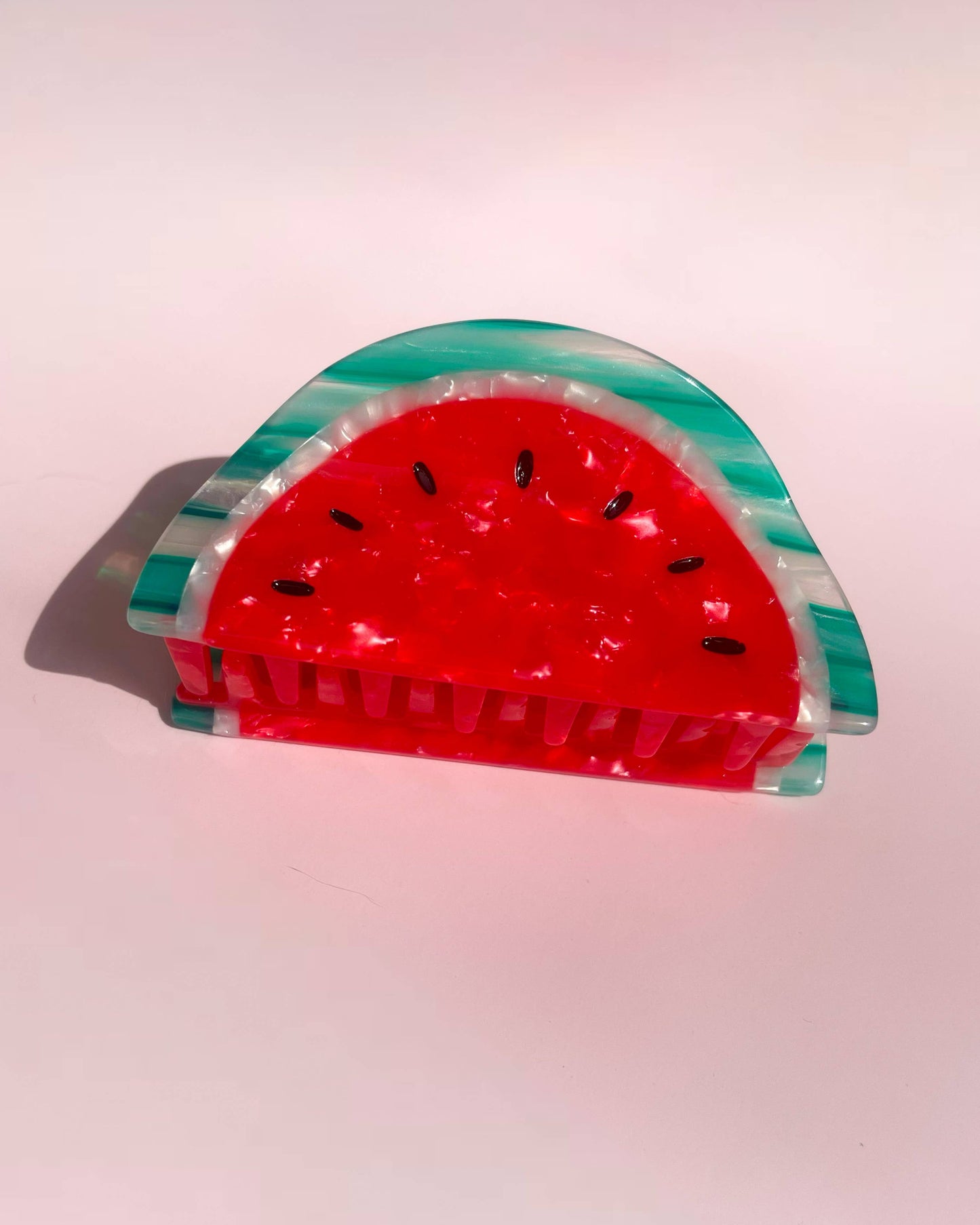 Red and green watermelon-shaped hair clip laying on a pink background