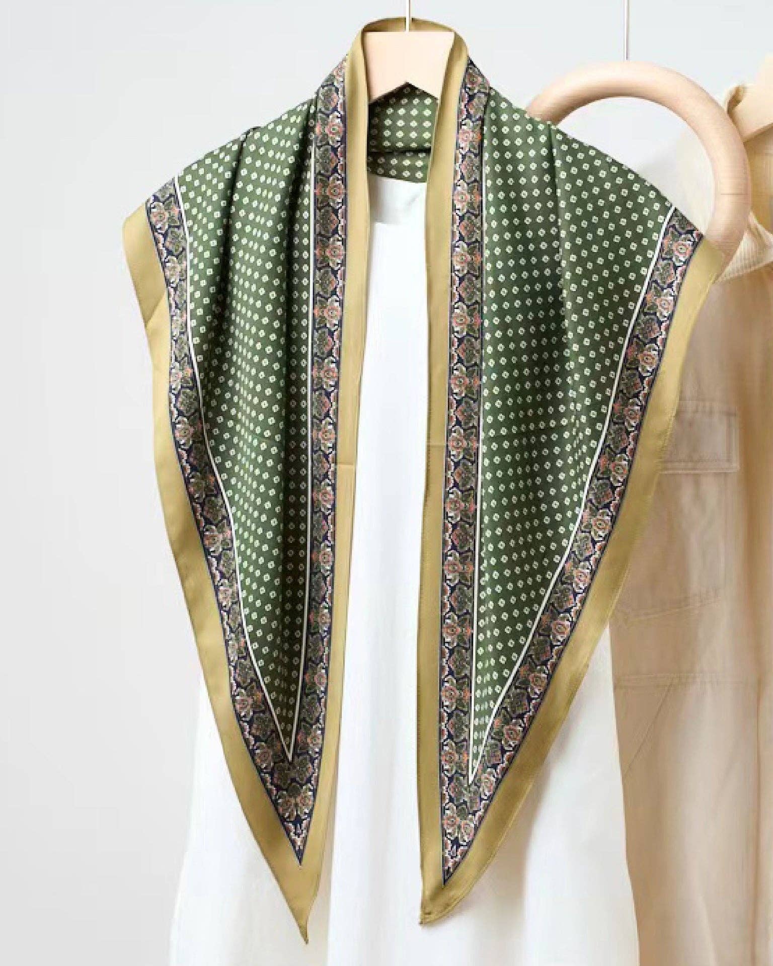 Green patterned scarf draped over a white shirt with beige jacket on a white background
