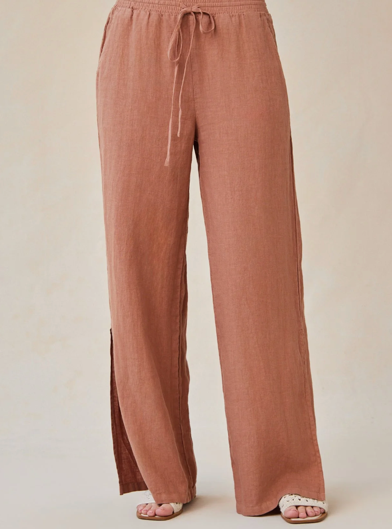 Model is wearing Bella Dahl Side Slit Wide Leg Pant in Terracotta Brown with white sandals on a off-white background