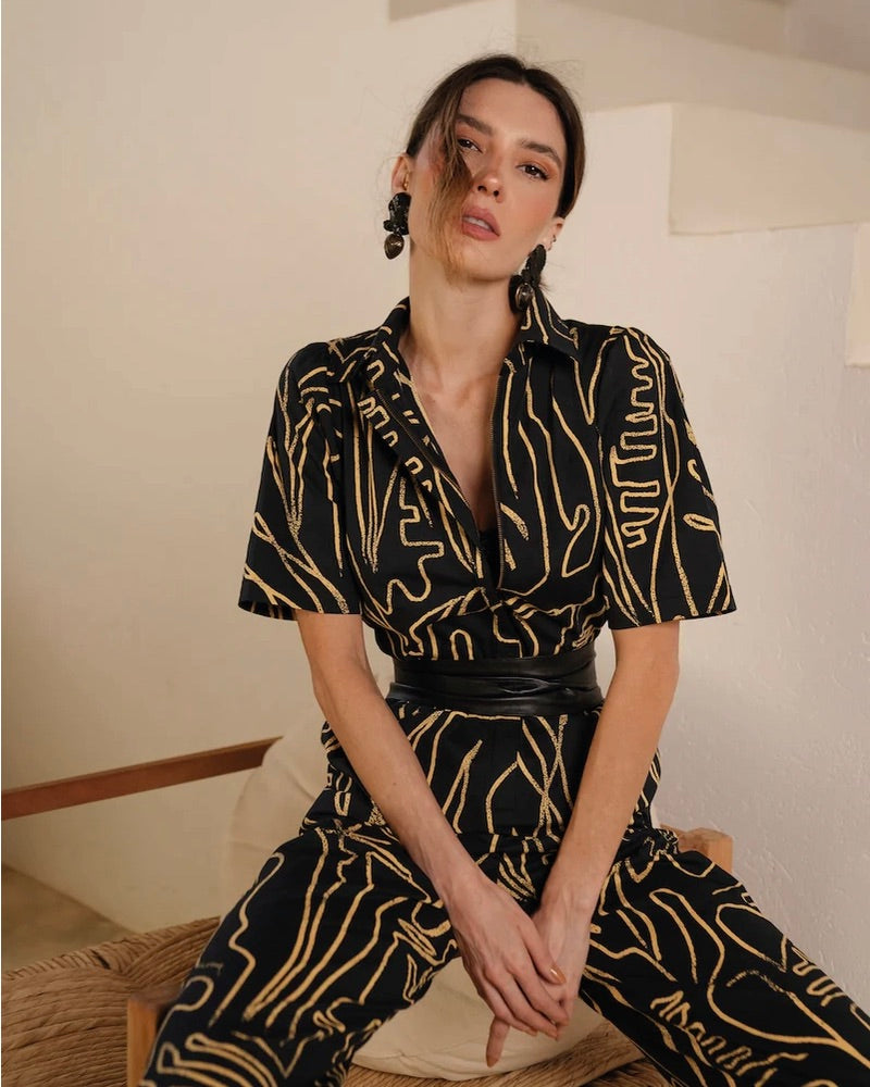 Model wearing a jumpsuit styled with the black leather Ada wrap belt sitting on a cushion with a neutral background