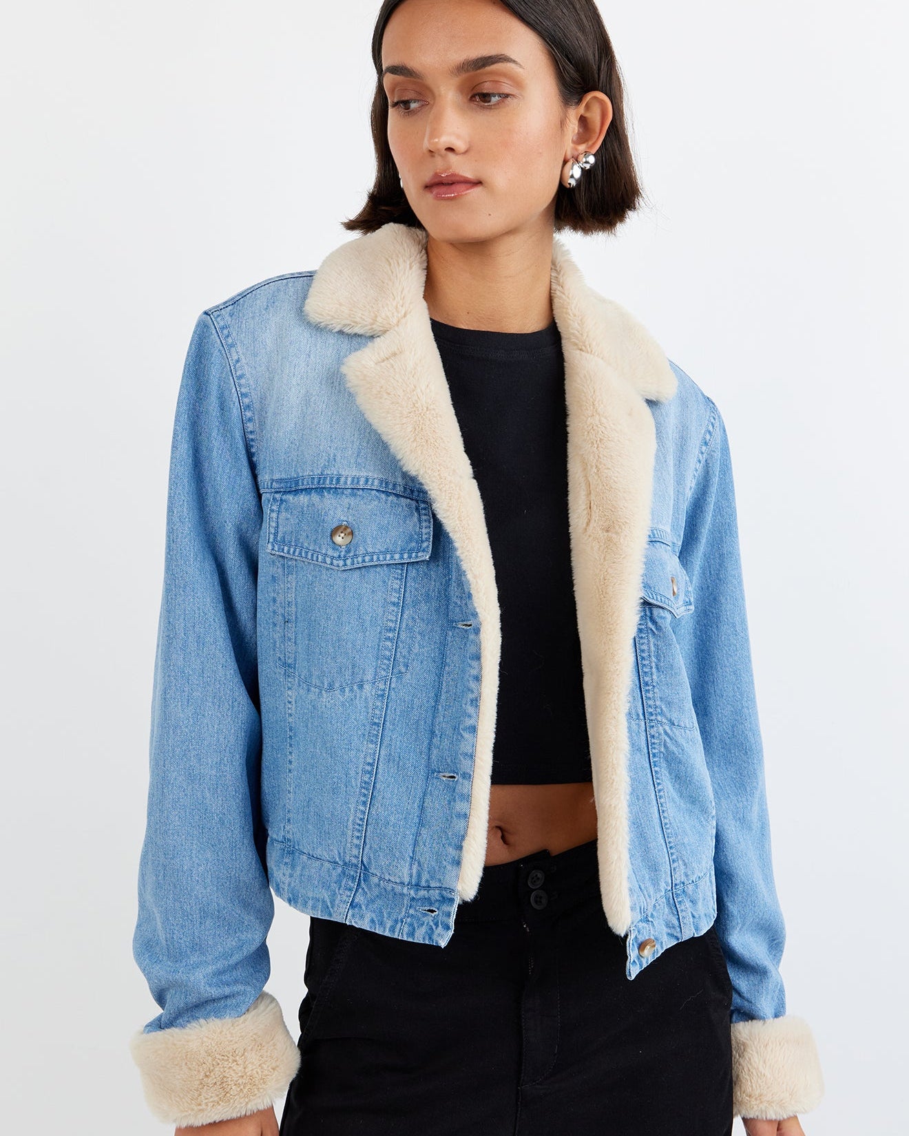 Woman wearing a denim jacket with white fur lining on a plain background