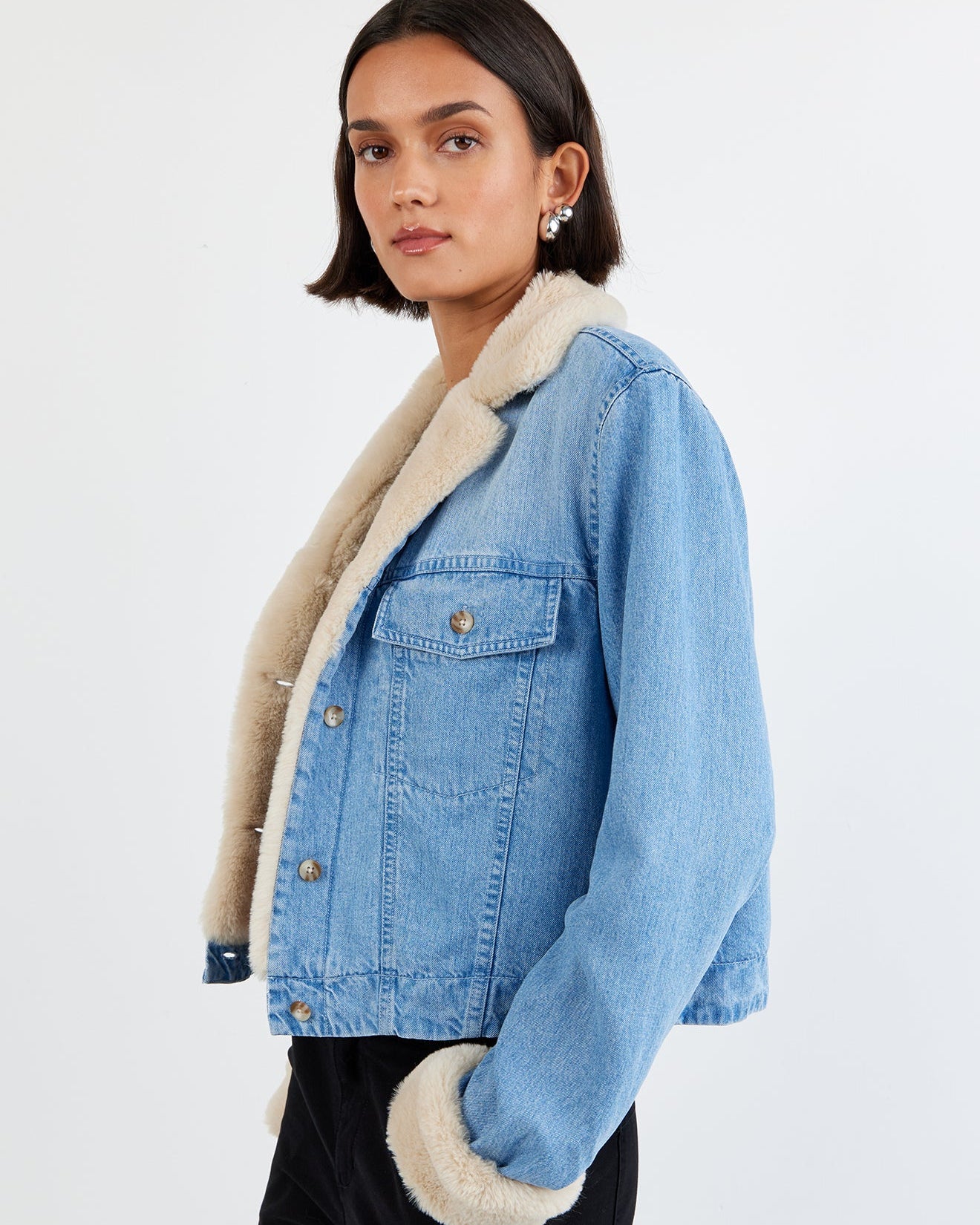 Woman wearing a blue denim jacket with beige sherpa lining on a white background