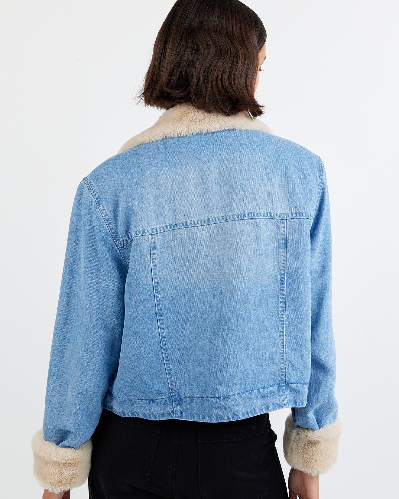 Person wearing a blue denim jacket with fur trim on a white background