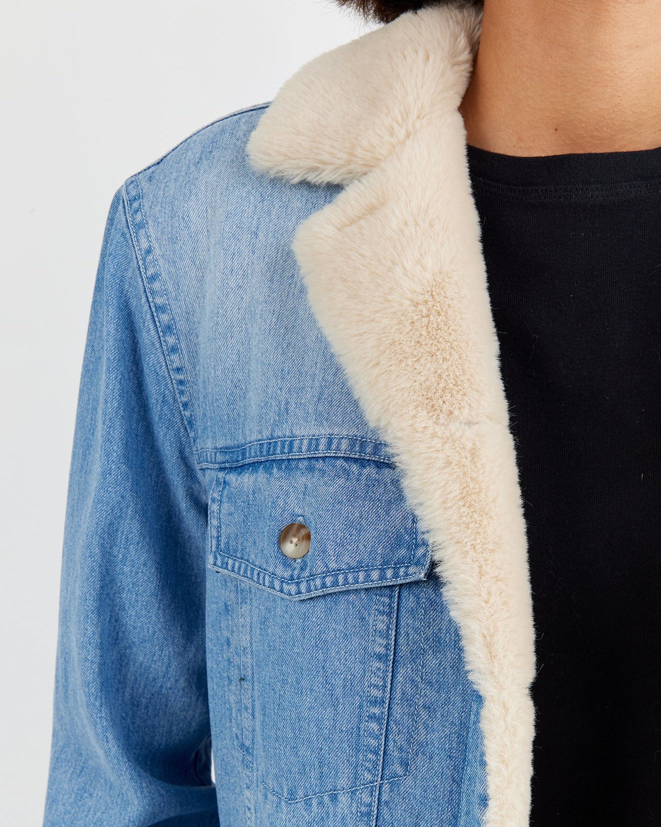 Blue denim jacket with white fur lining on a plain background