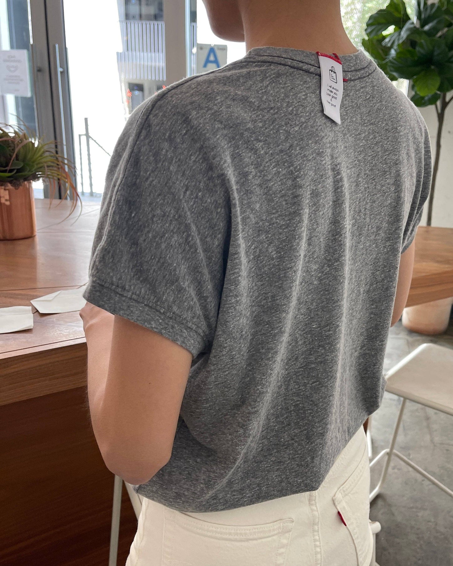 Person wearing a gray t-shirt with a brand tag in an indoor setting