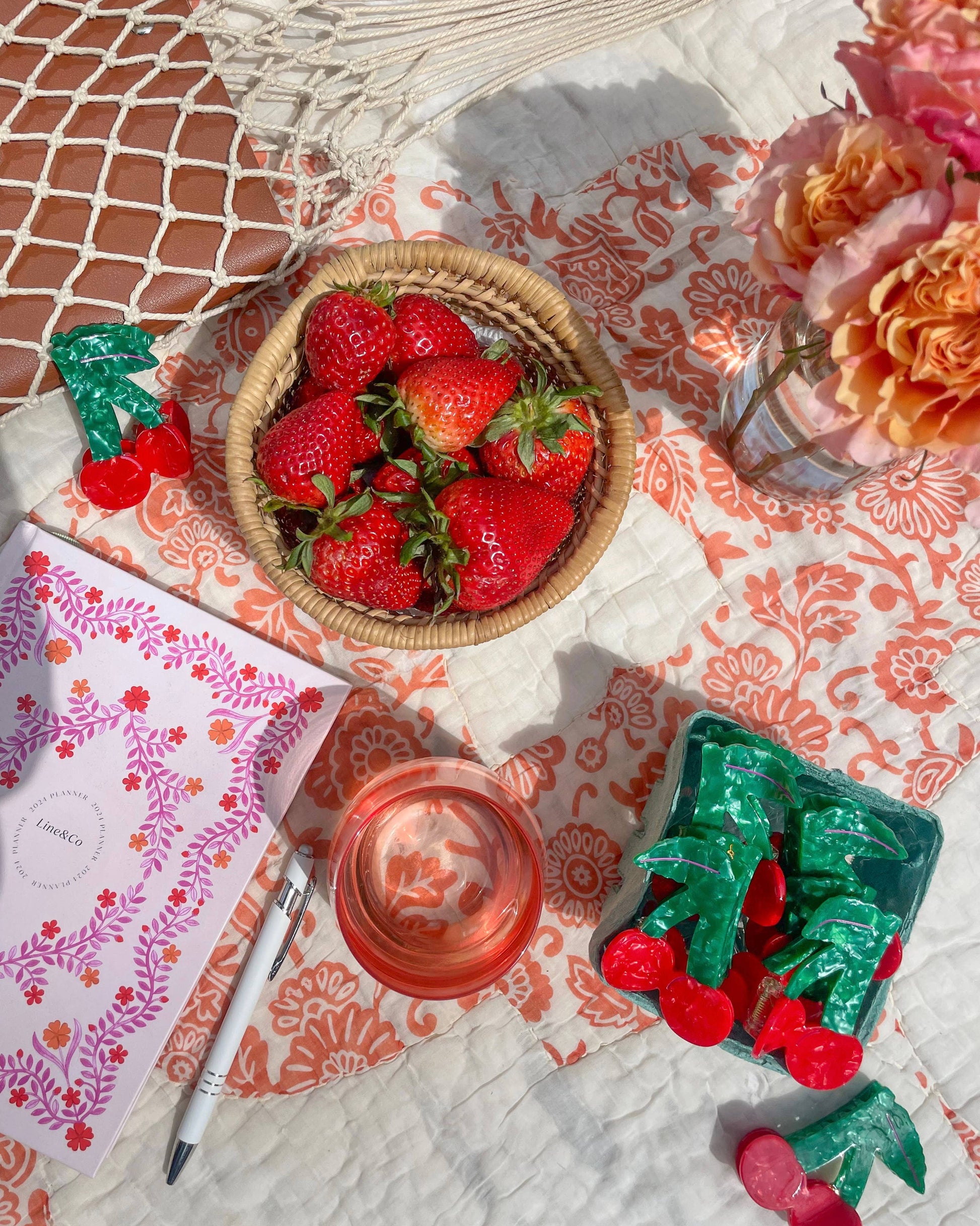 Cherries in a small green basket along with other decorative items on a patterned surface