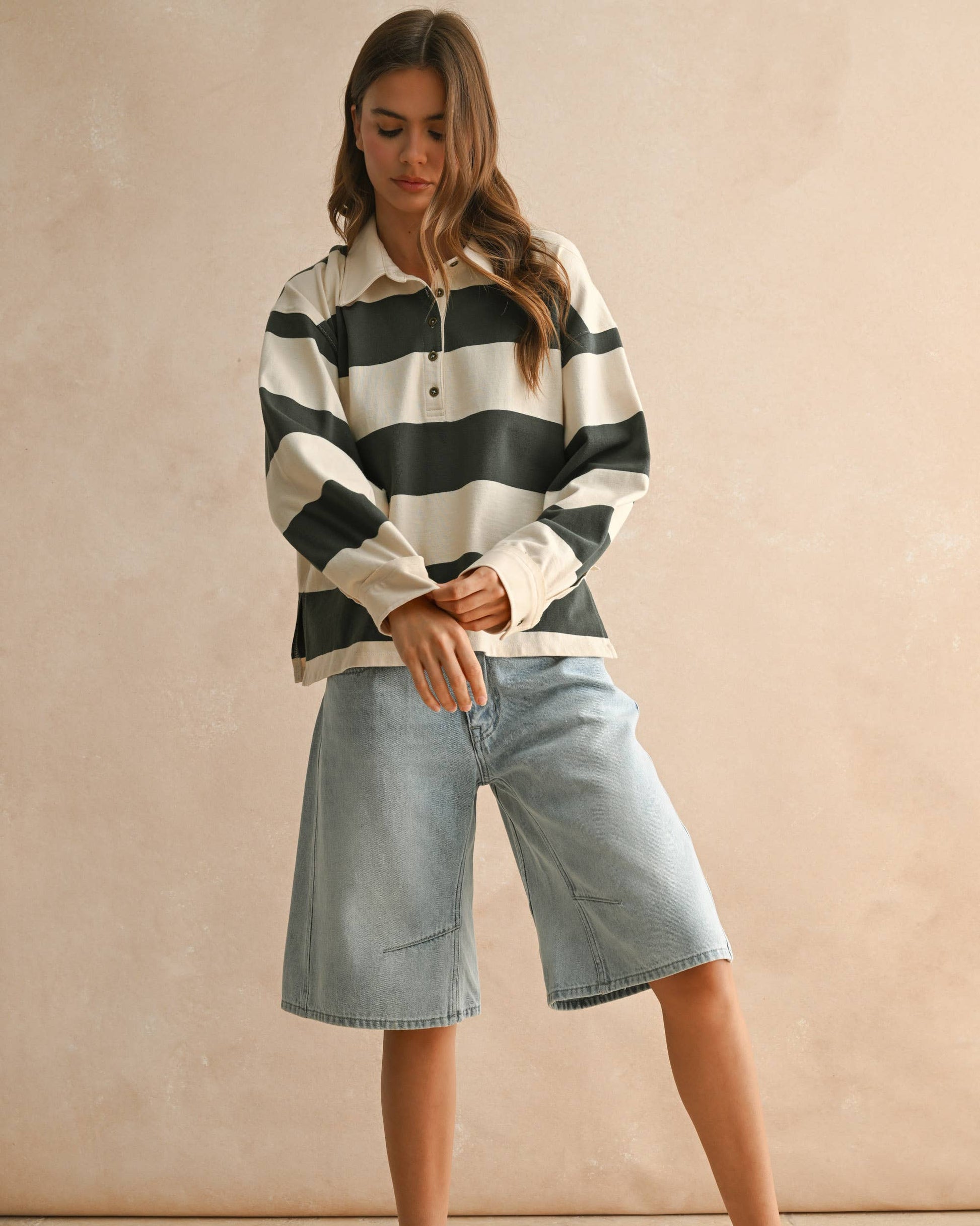 Woman wearing a striped shirt and denim shorts against a beige background