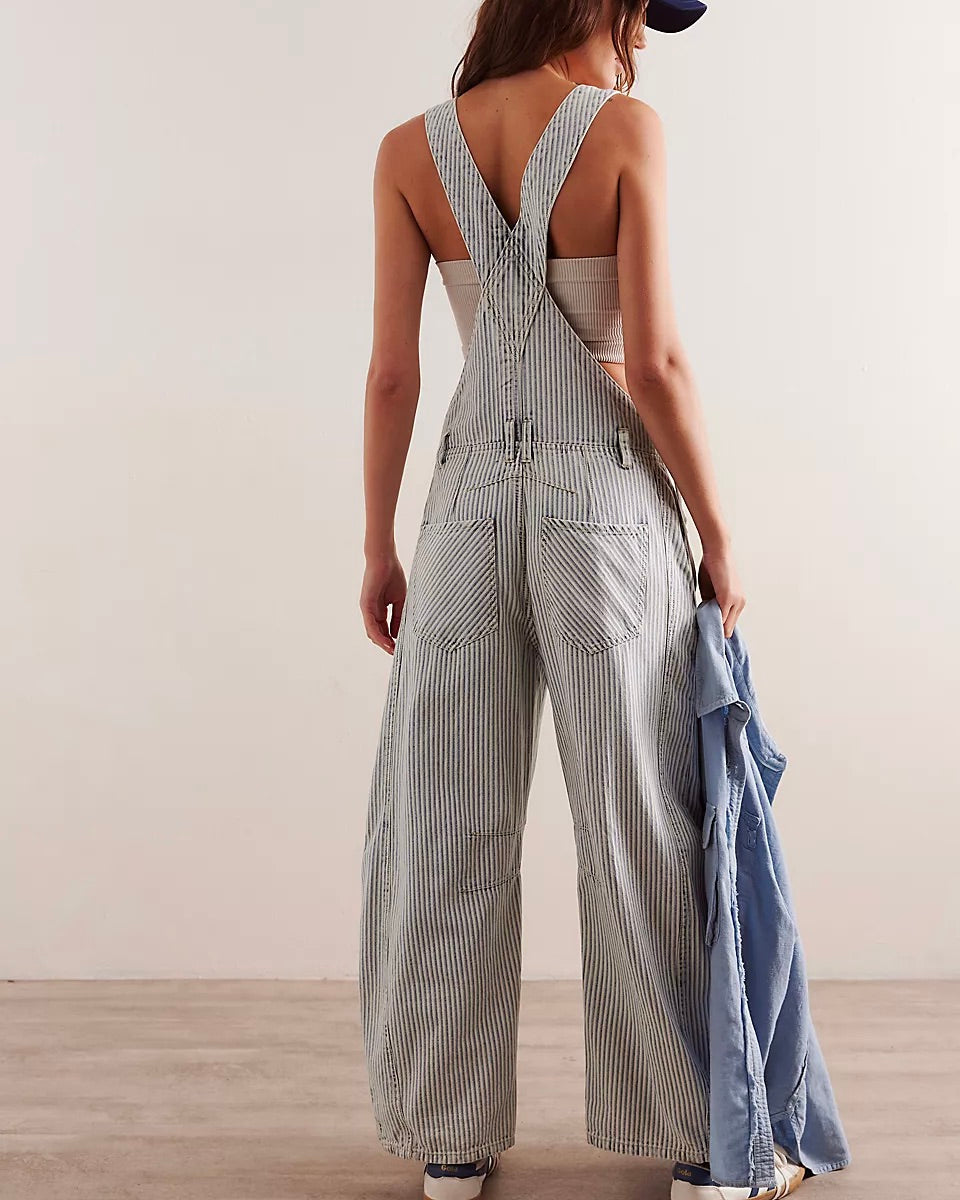 Back view of a model wearing the Free People Good Luck Stripe Overall standing on a wood floor in front of a white wall.