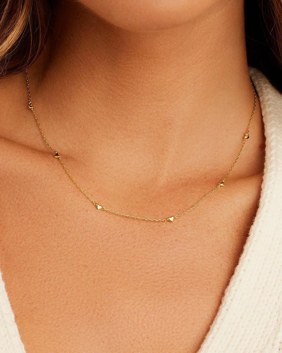 Gold necklace on a person's neck with a neutral background