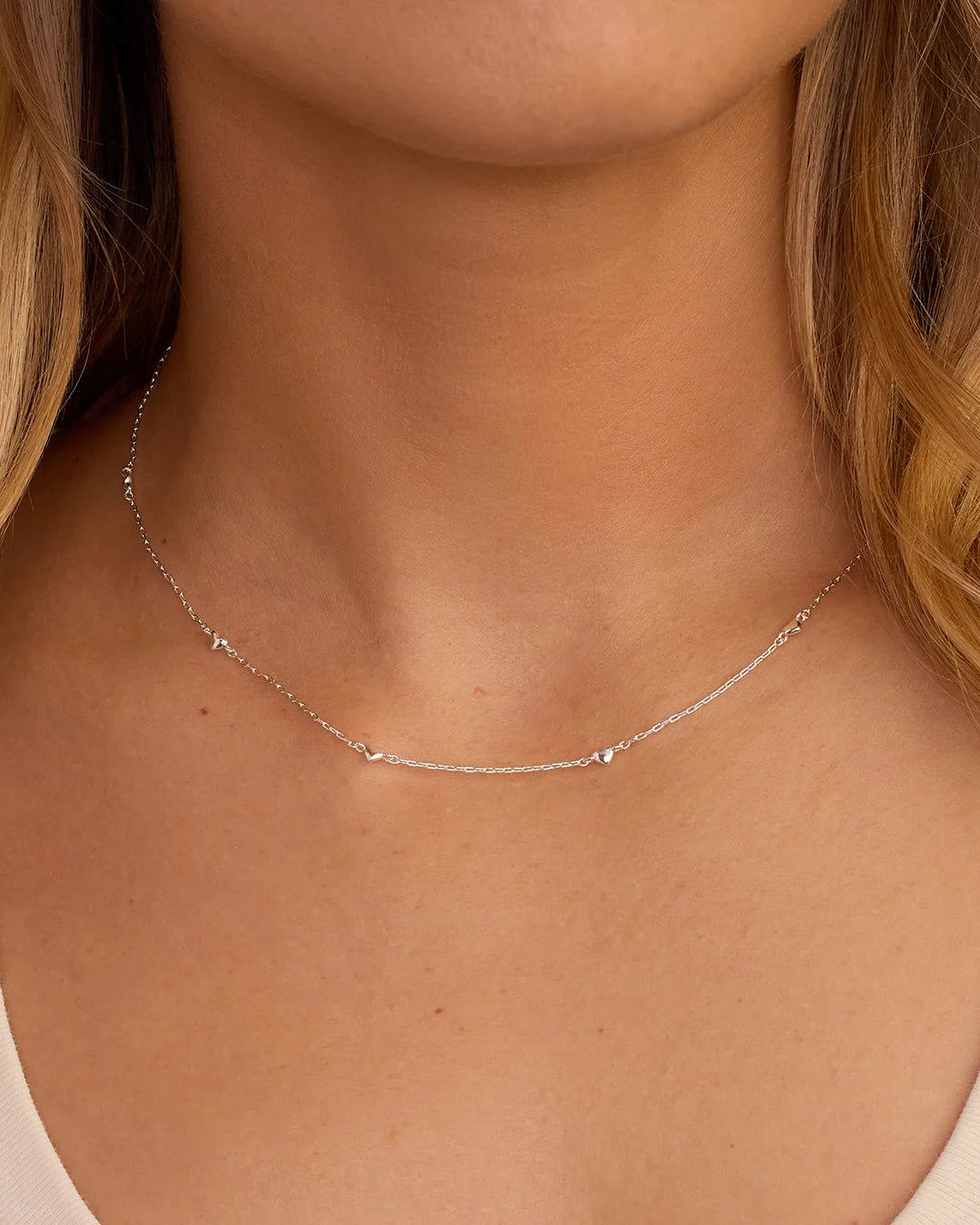 Silver necklace on a person's neck with a neutral background