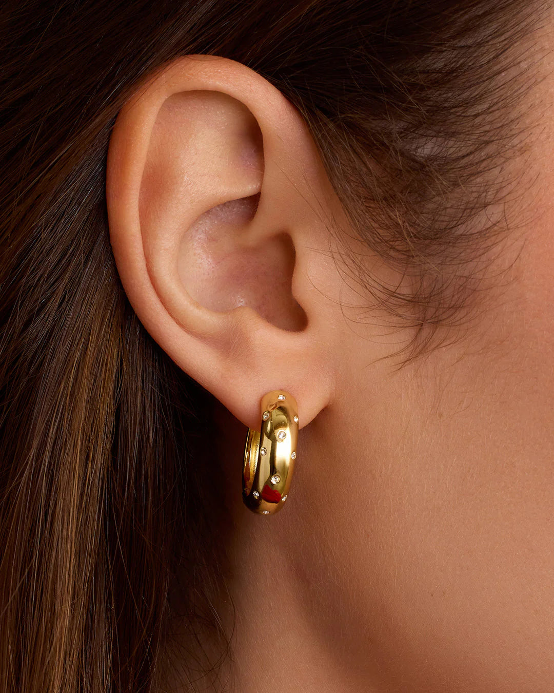 Close-up of an ear wearing a gold hoop earring with red and black accents.
