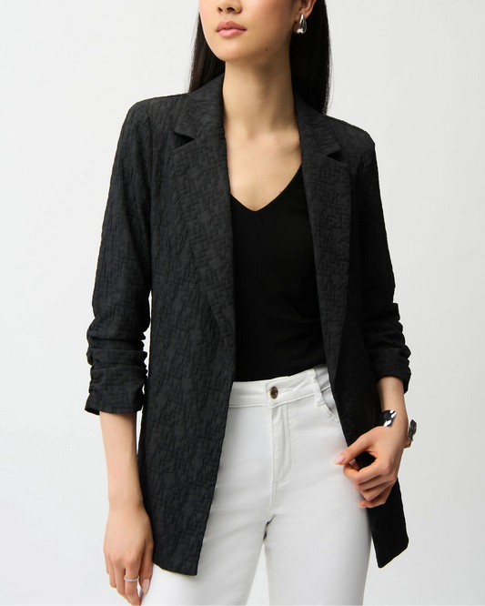 Woman wearing a navy blazer over a black top and white pants on a light gray background