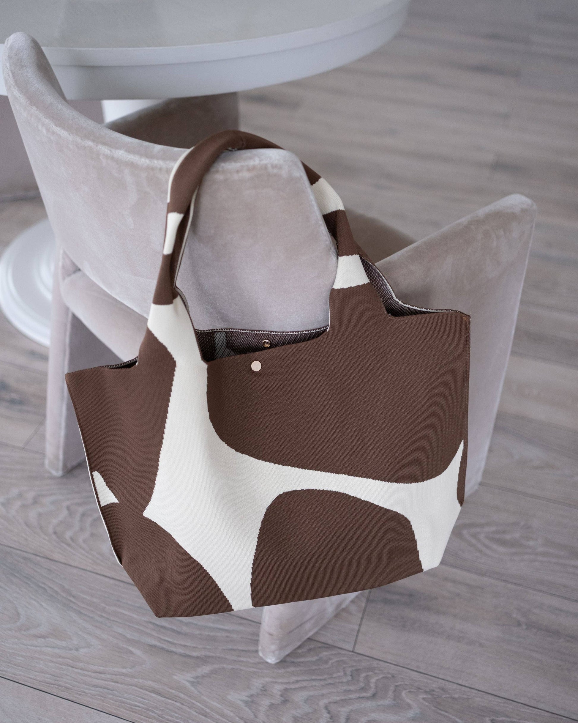 Brown and white patterned bag on a chair in a room with a table and plant.