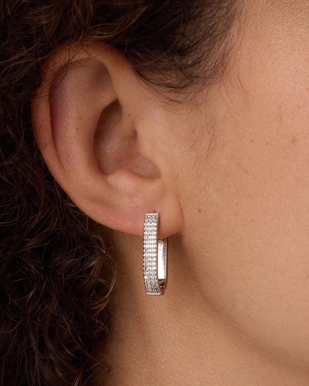 Close-up of an ear wearing a silver hoop earring with clear stones.