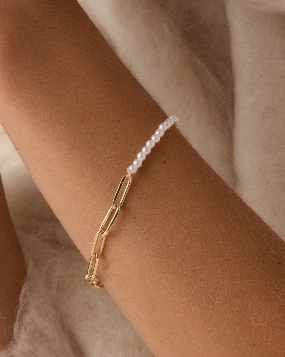 Gold bracelet with a pearl charm on a wrist against a neutral background