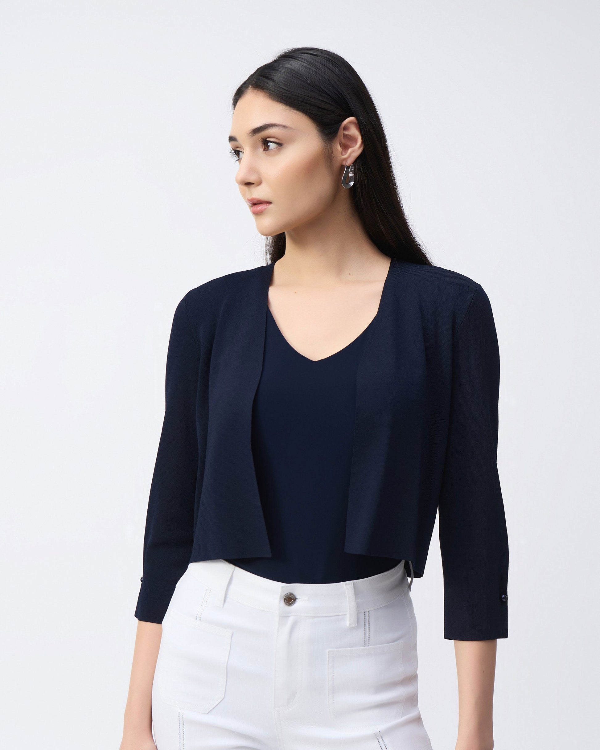 Model in a navy cover up with white pants in front of a white background