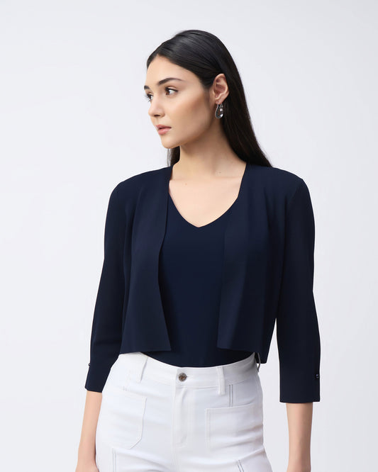 Model in a navy cover up with white pants in front of a white background