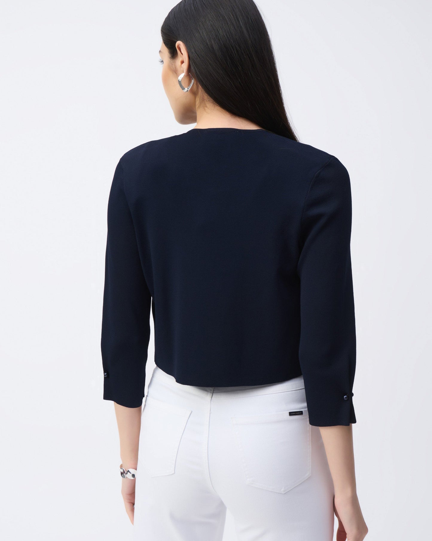 Back view of a navy coverup on a model  wearing white pants with a white background.
