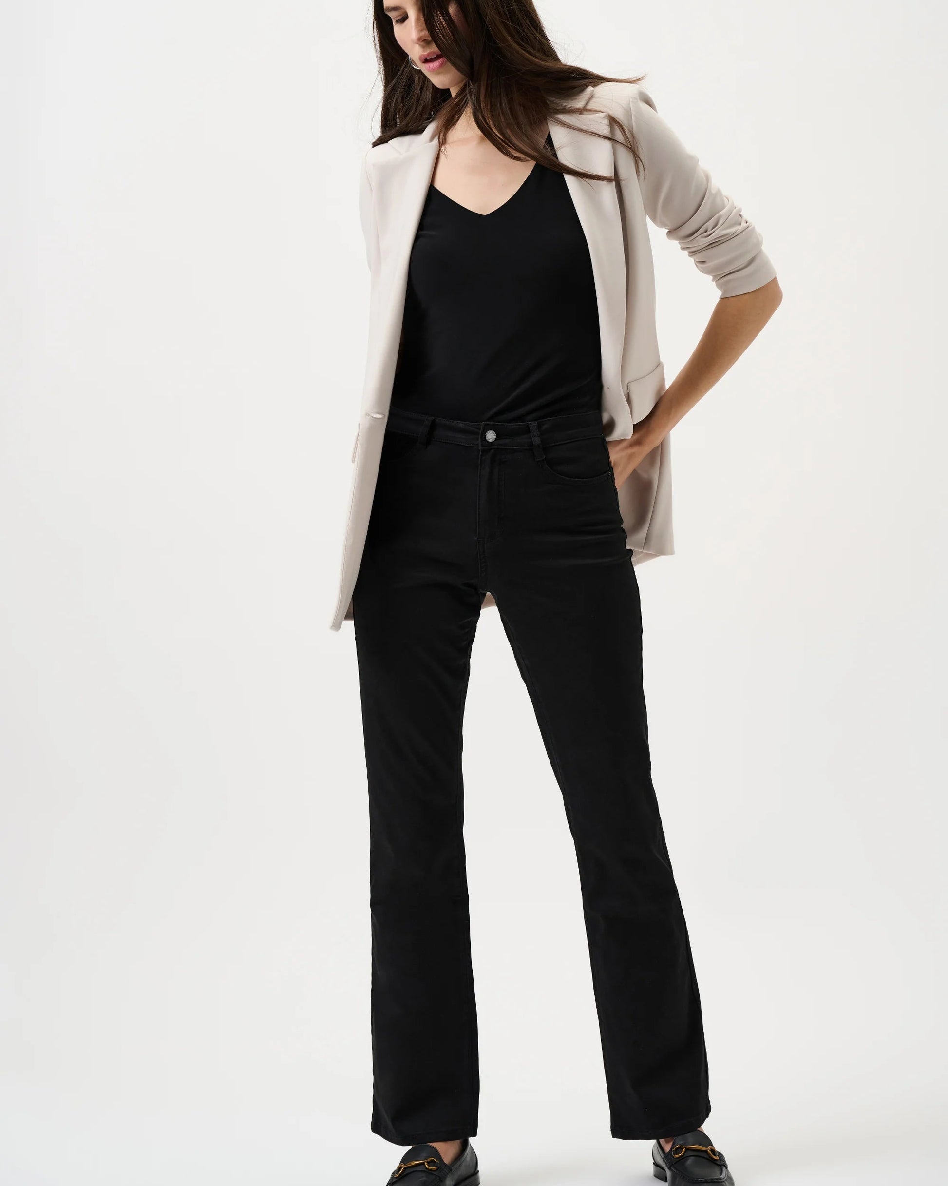 Woman wearing a beige blazer, black top, and black pants on a white background