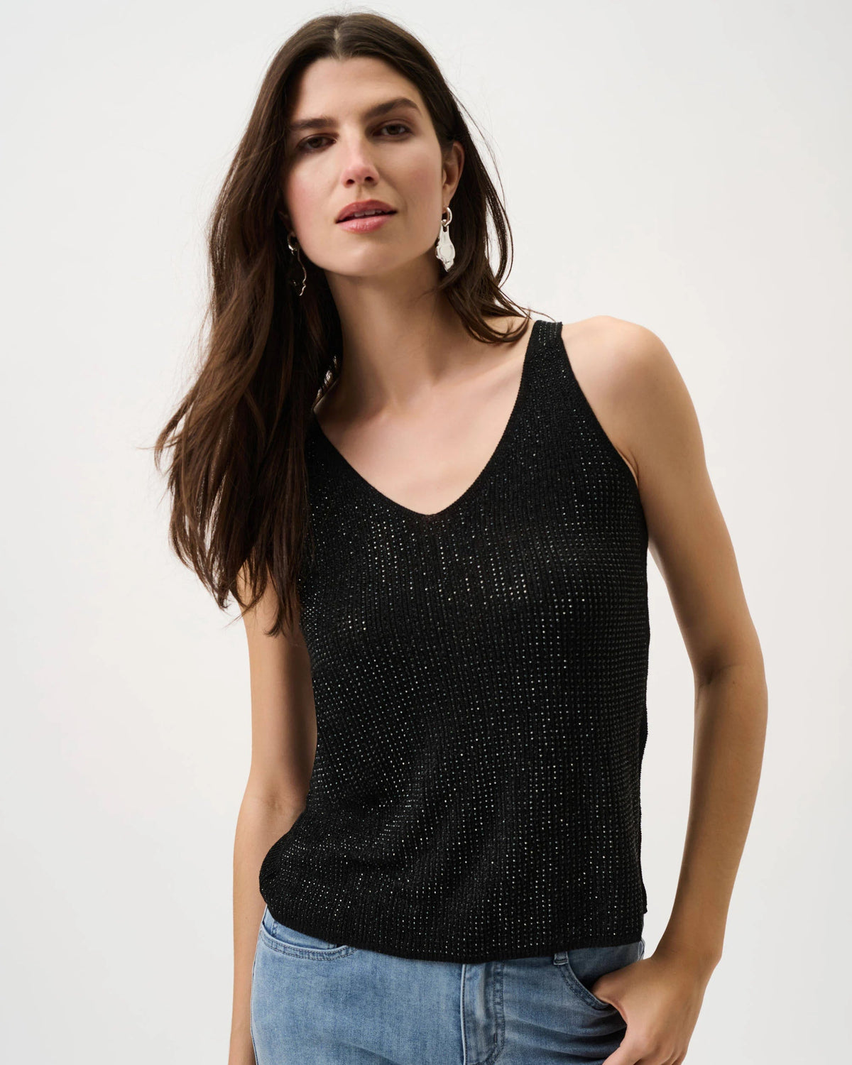 Woman wearing a black tank top and blue jeans on a white background