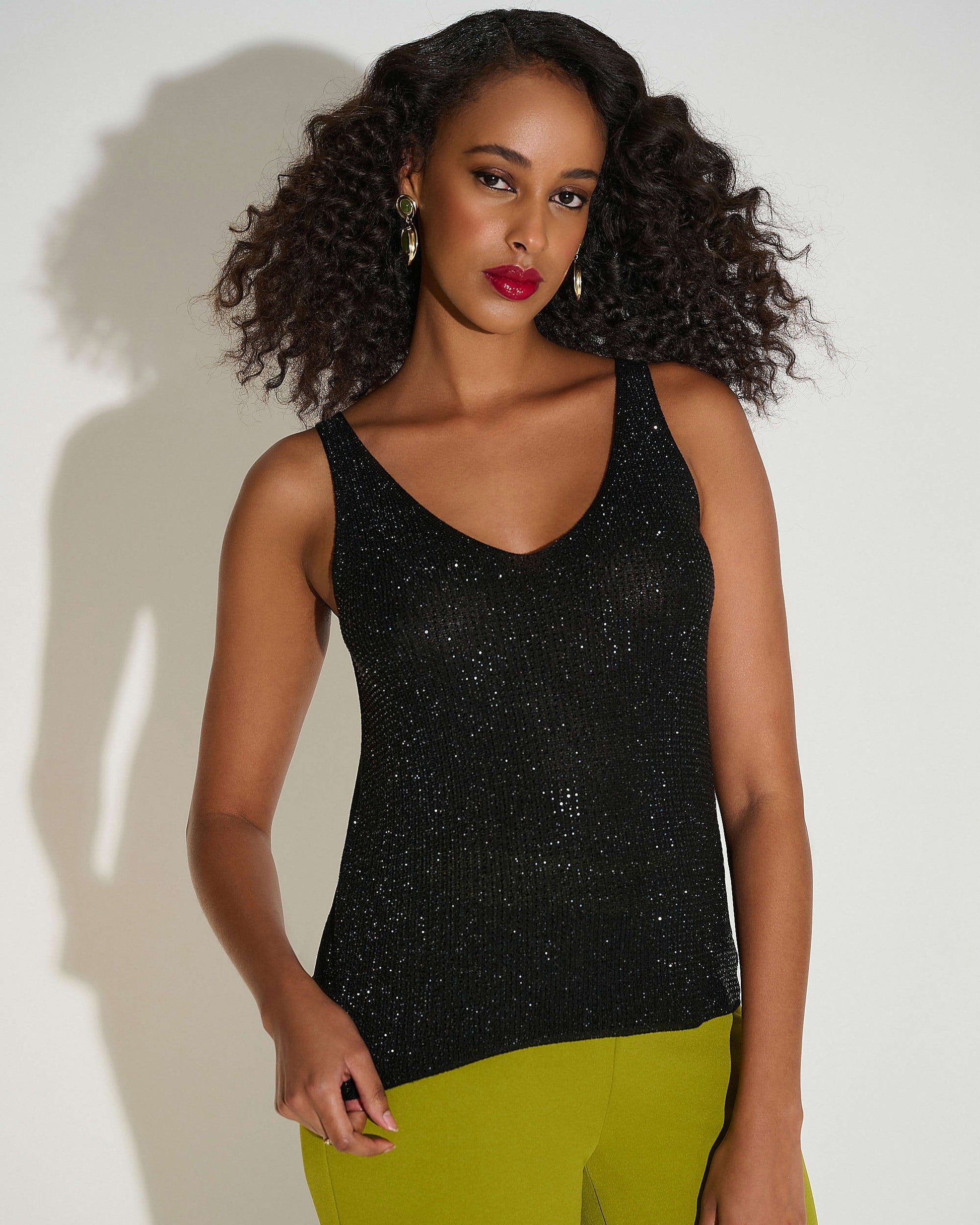 Woman wearing a black sleeveless top and green pants against a white background