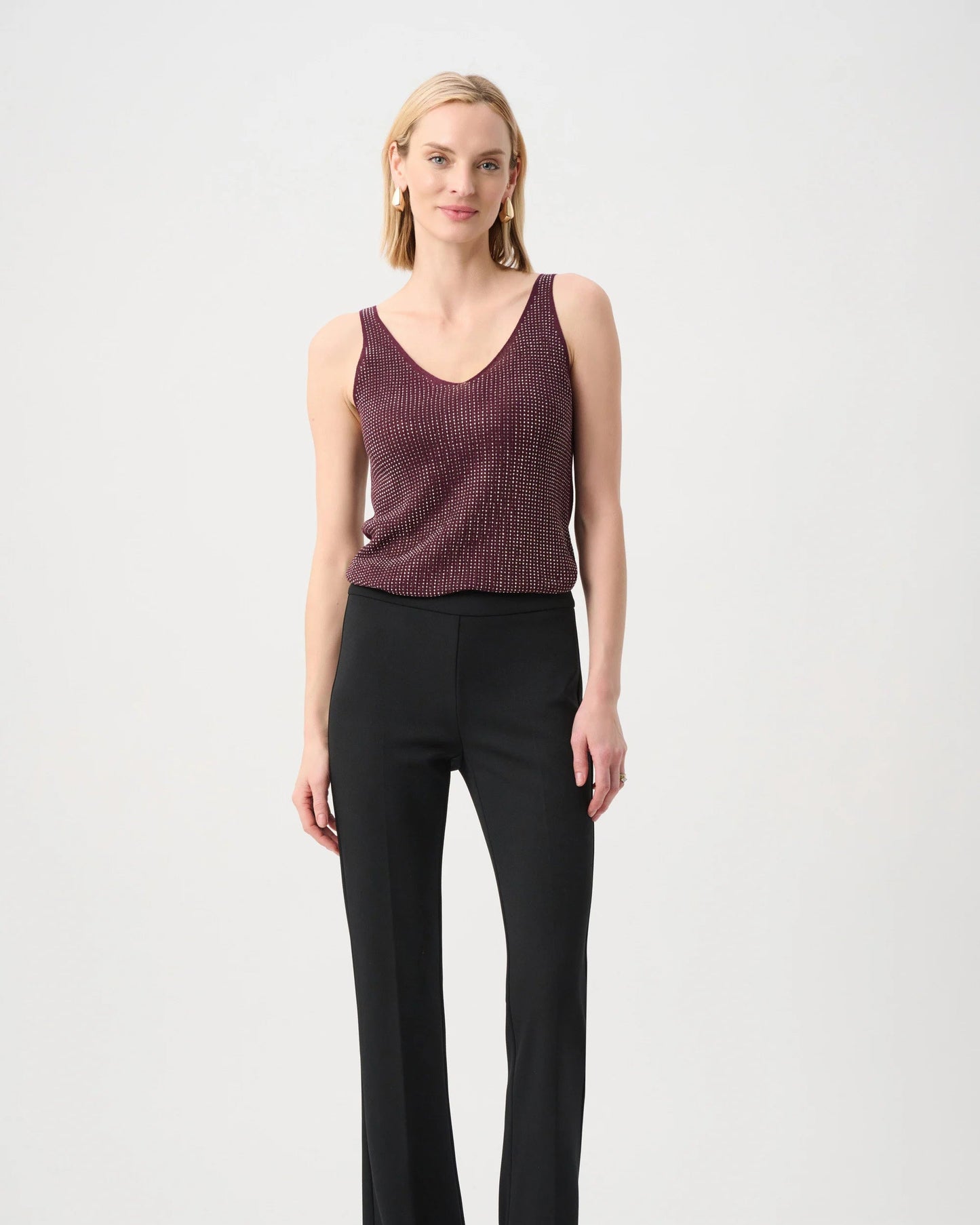 Woman wearing a maroon sleeveless top and black pants on a white background