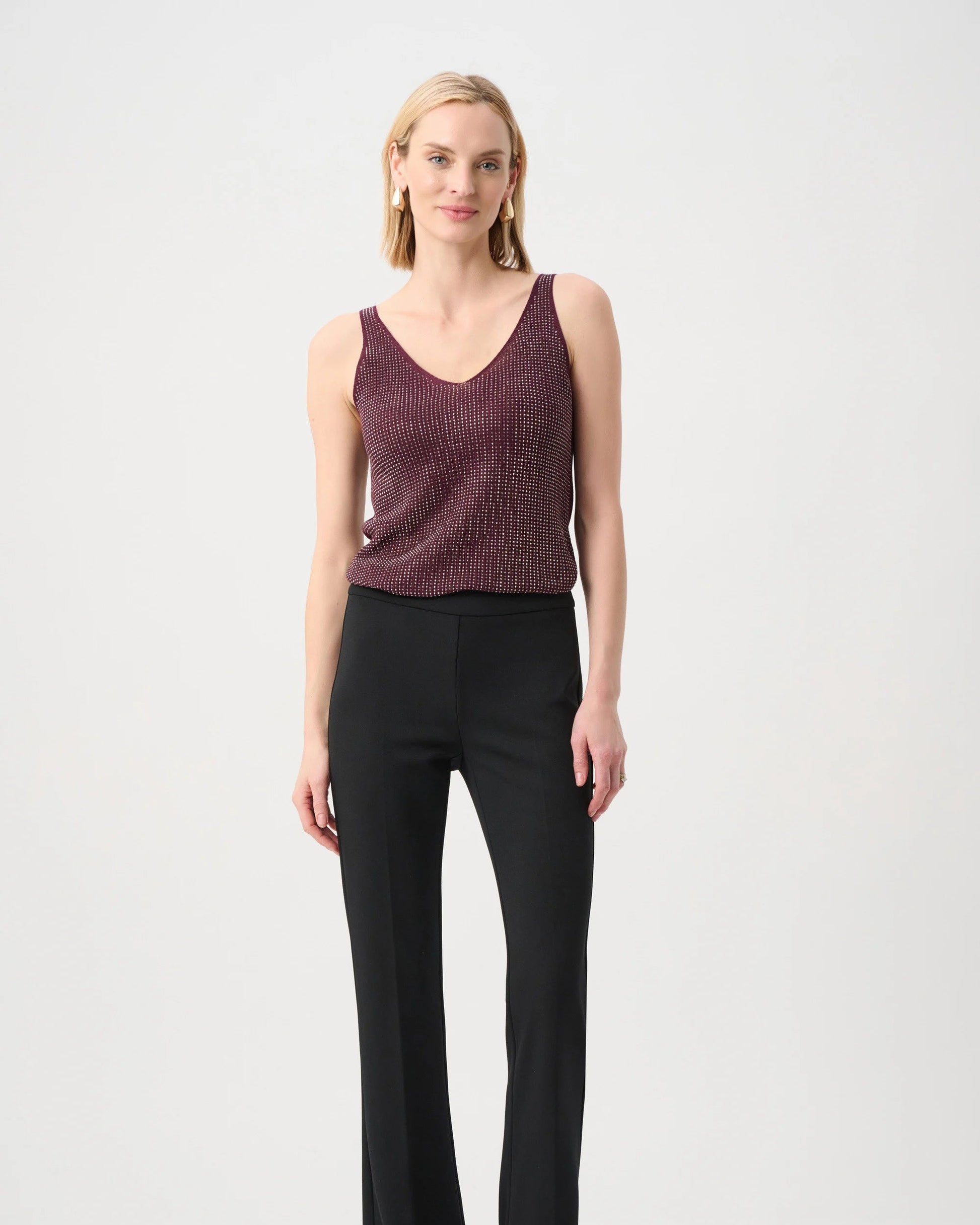 Woman wearing a maroon sleeveless top and black pants on a white background