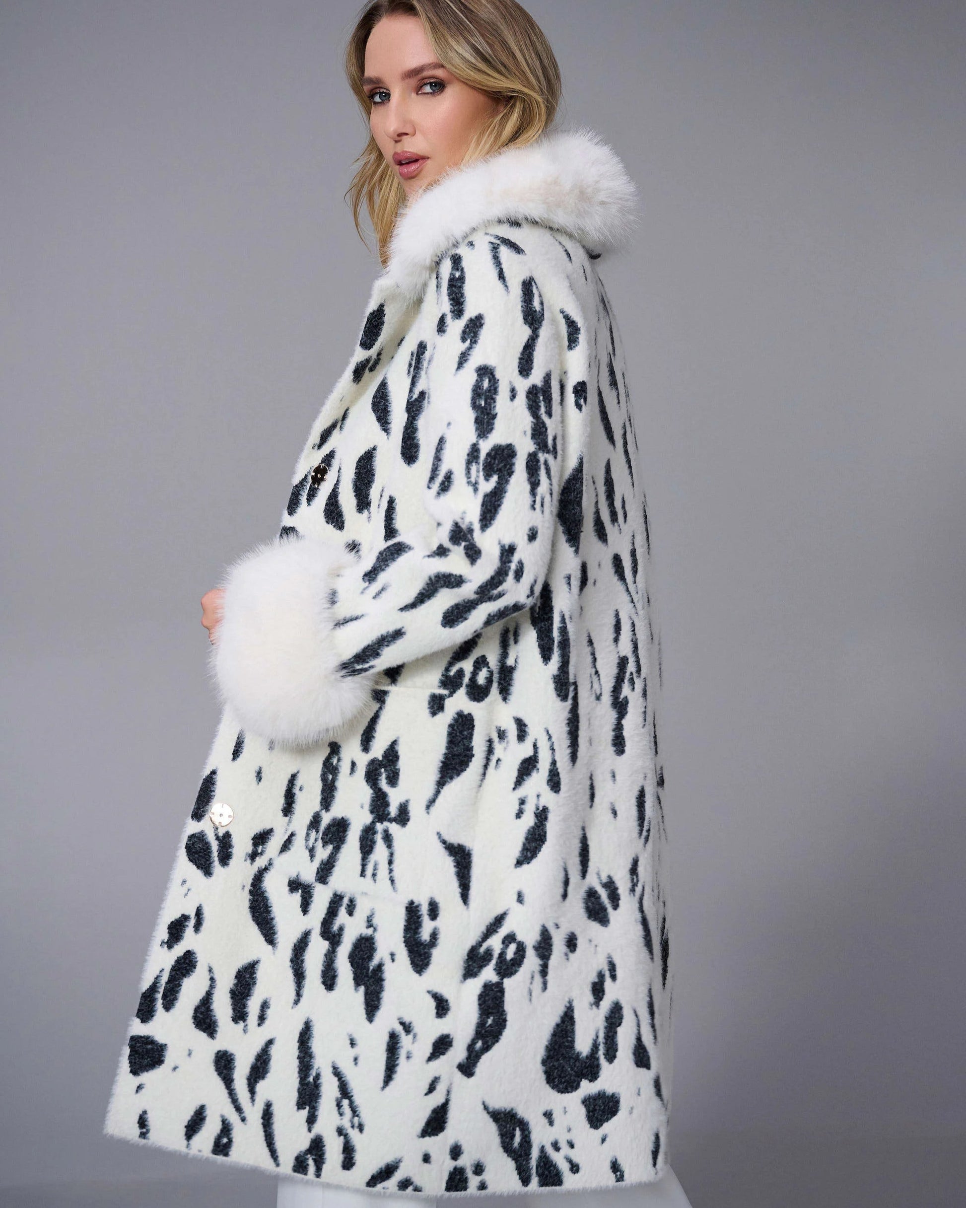 Woman wearing a white coat with black pattern and fur trim on a gray background