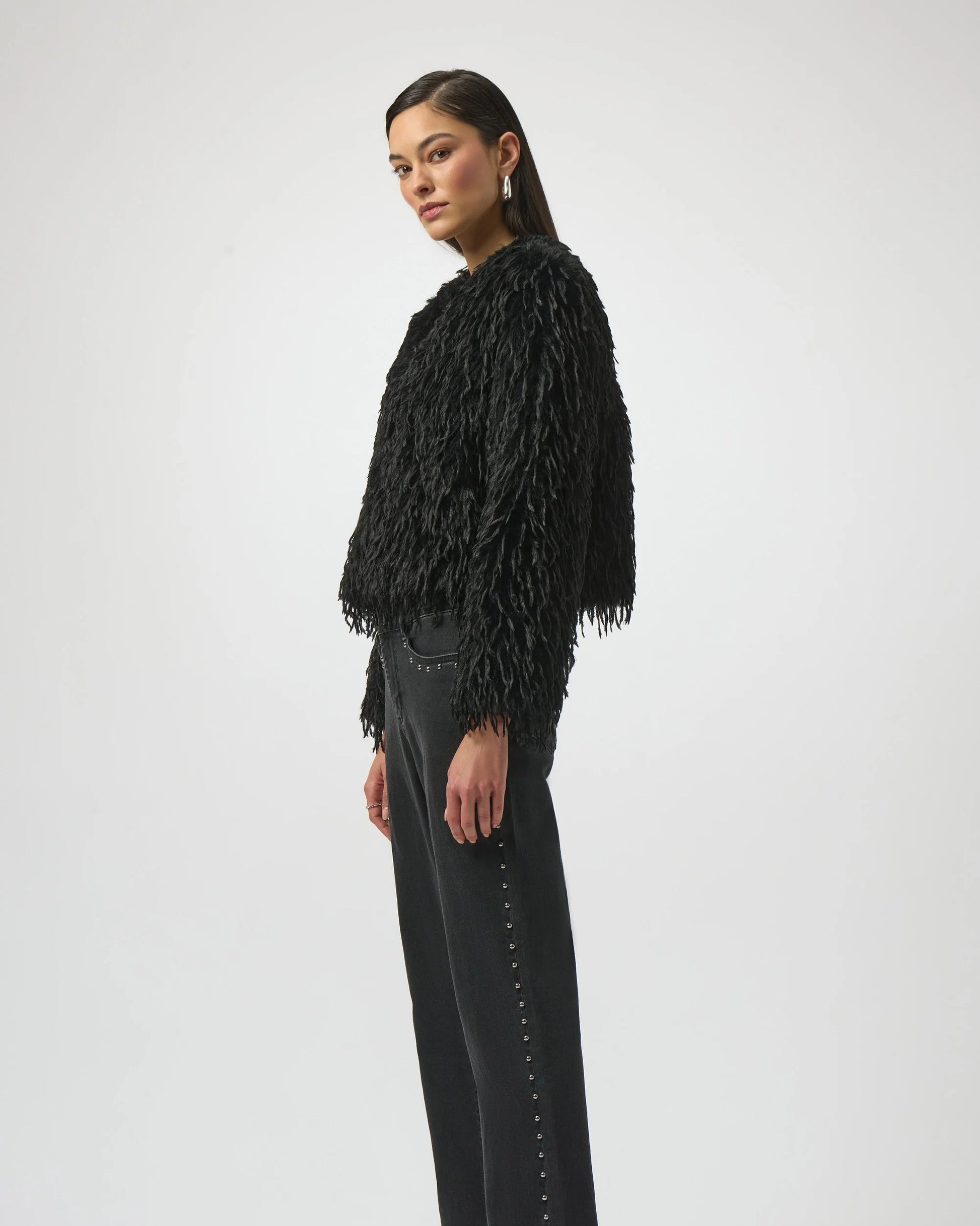 Woman wearing a black fringed jacket, black pants, and black boots on a white background