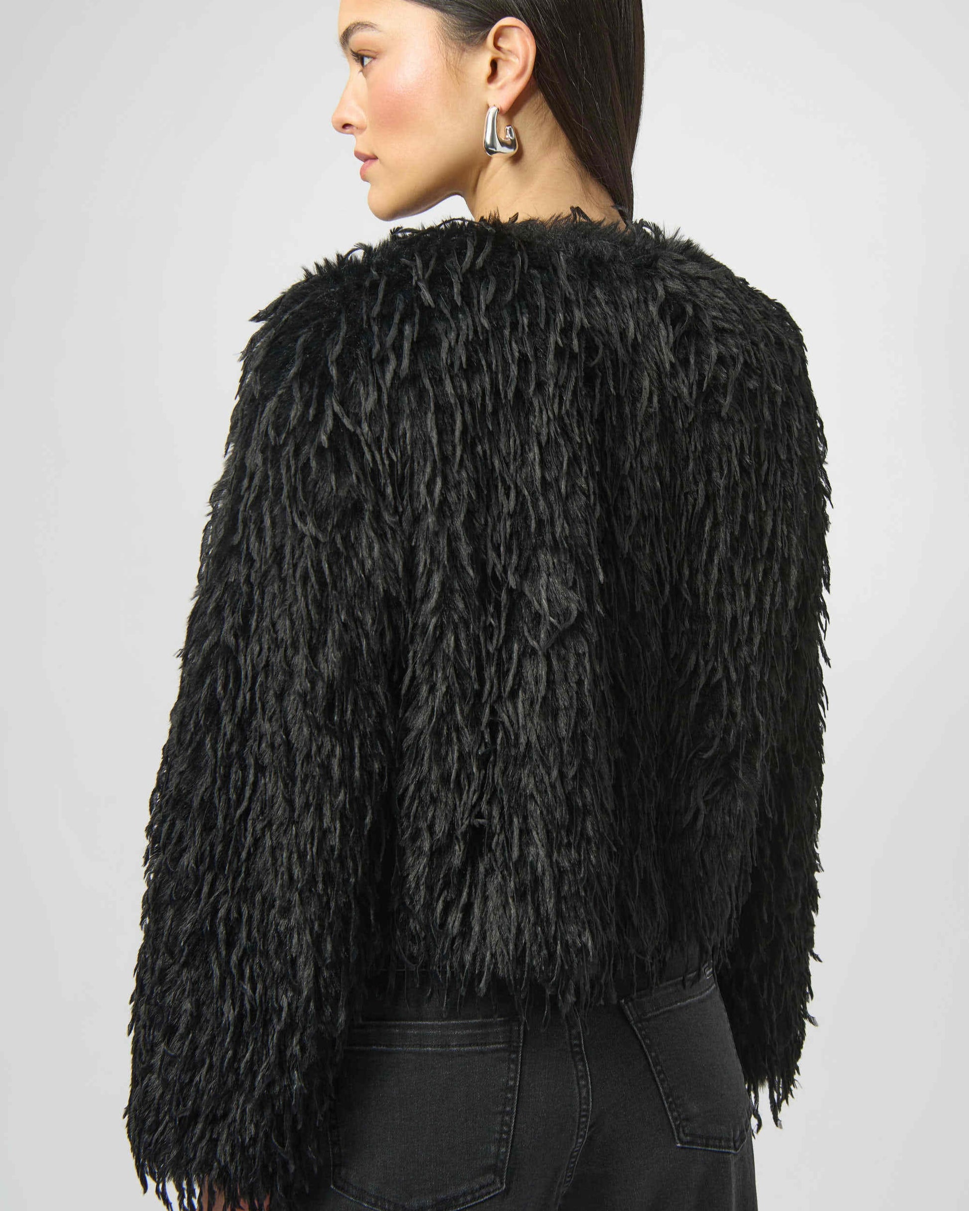 Person wearing a black faux fur jacket on a plain background