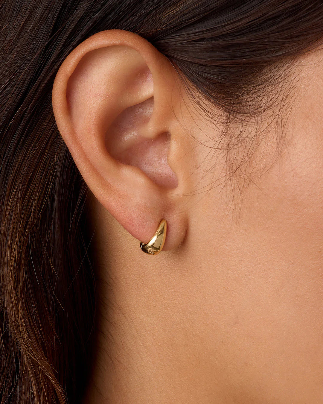 Gold hoop earring worn by a person with dark hair.