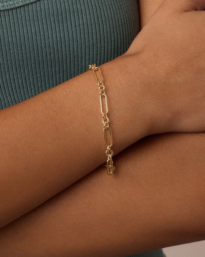 Gold chain bracelet on a wrist with a neutral background