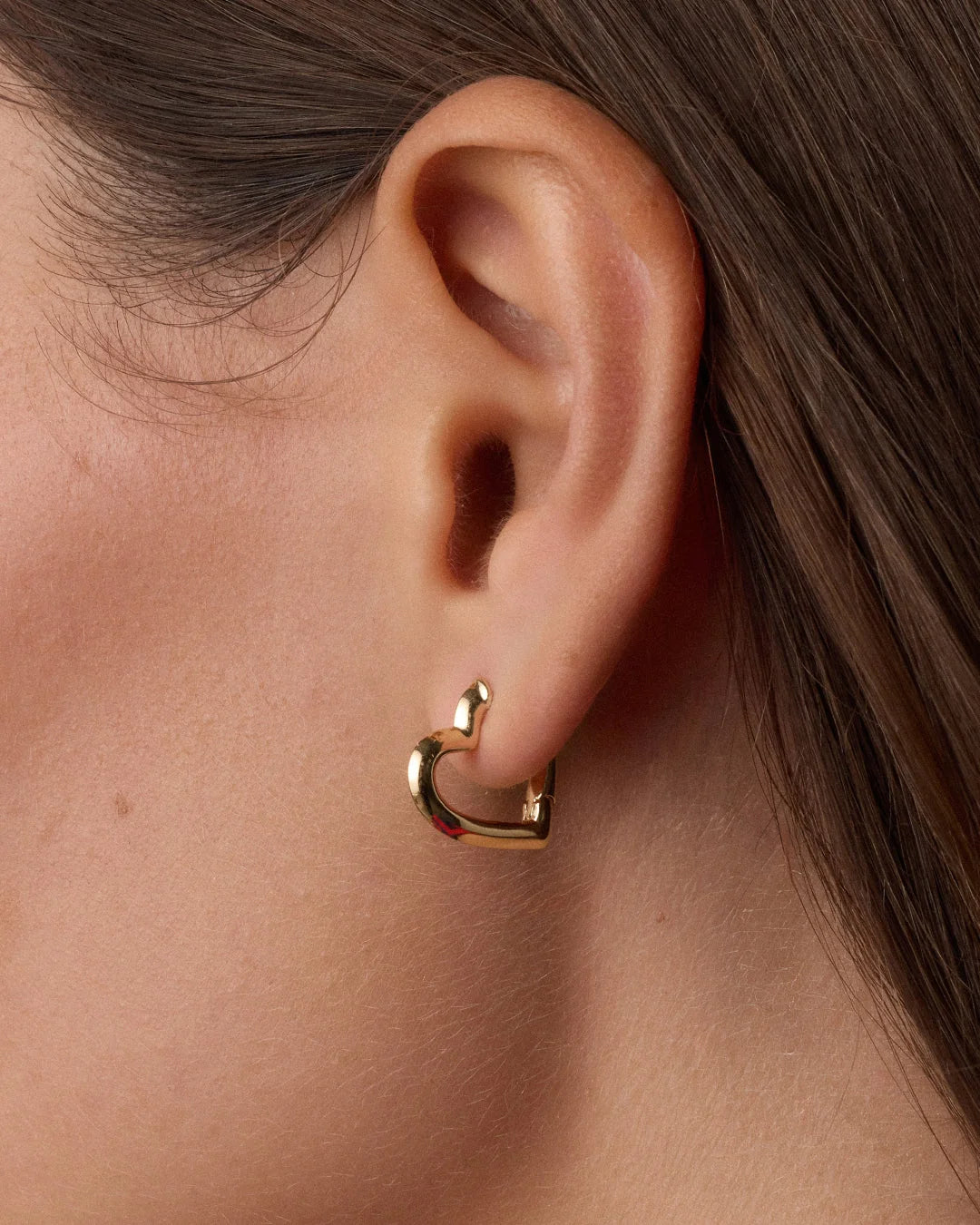 A close-up of a model's ear wearing a small gold huggie hoop earring.