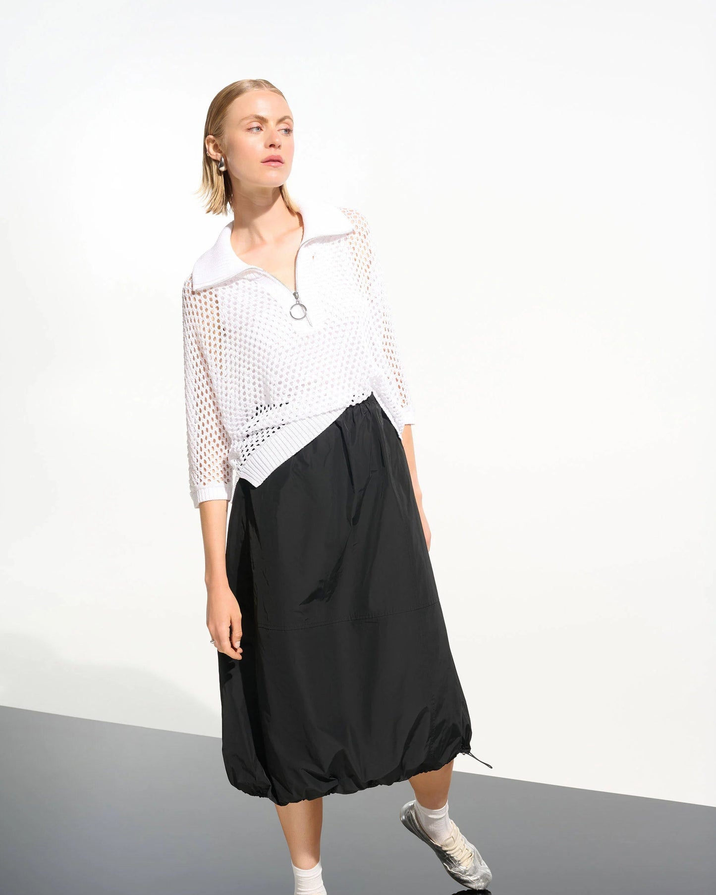 Person wearing a white top and black skirt on a plain background