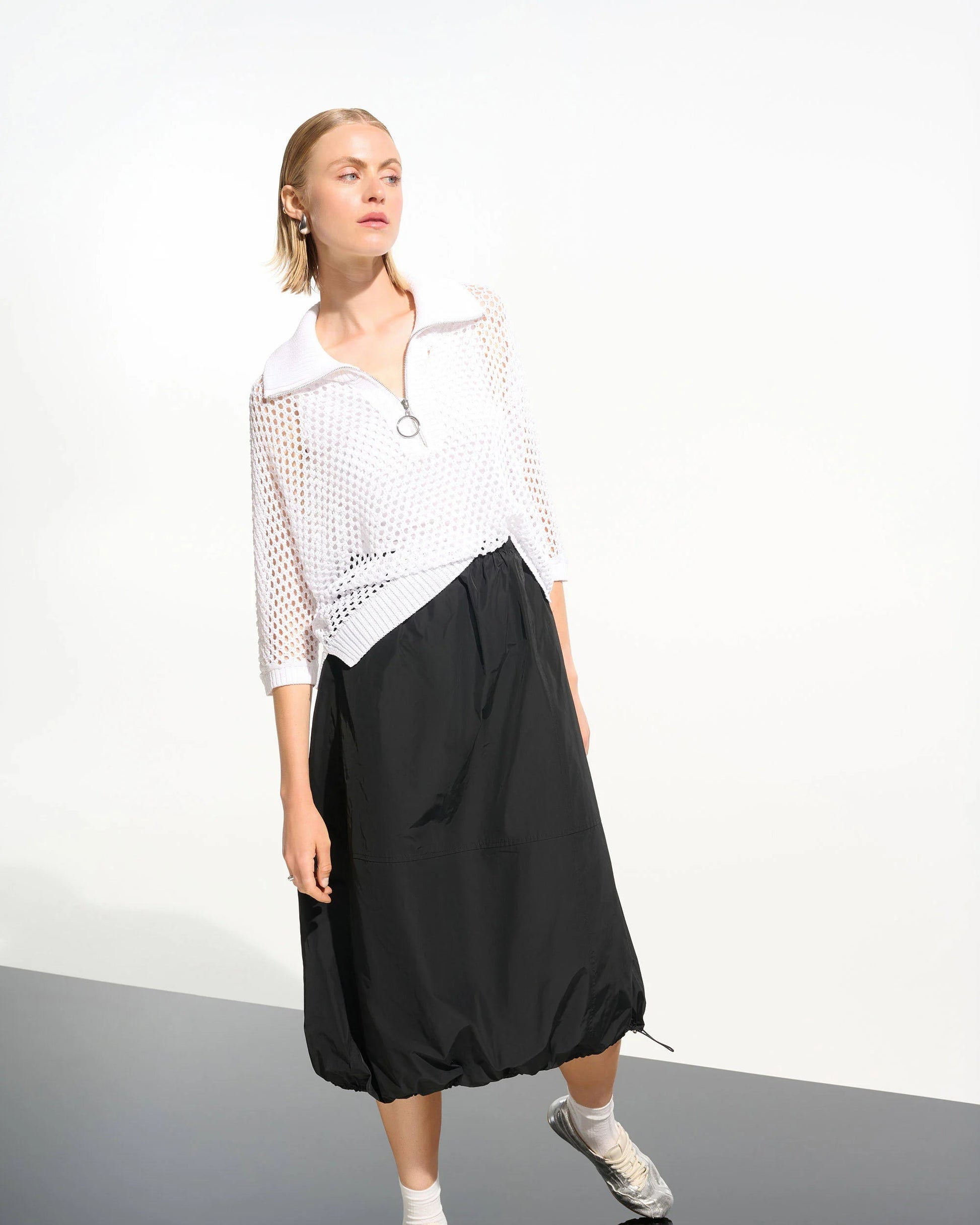 Person wearing a white top and black skirt on a plain background