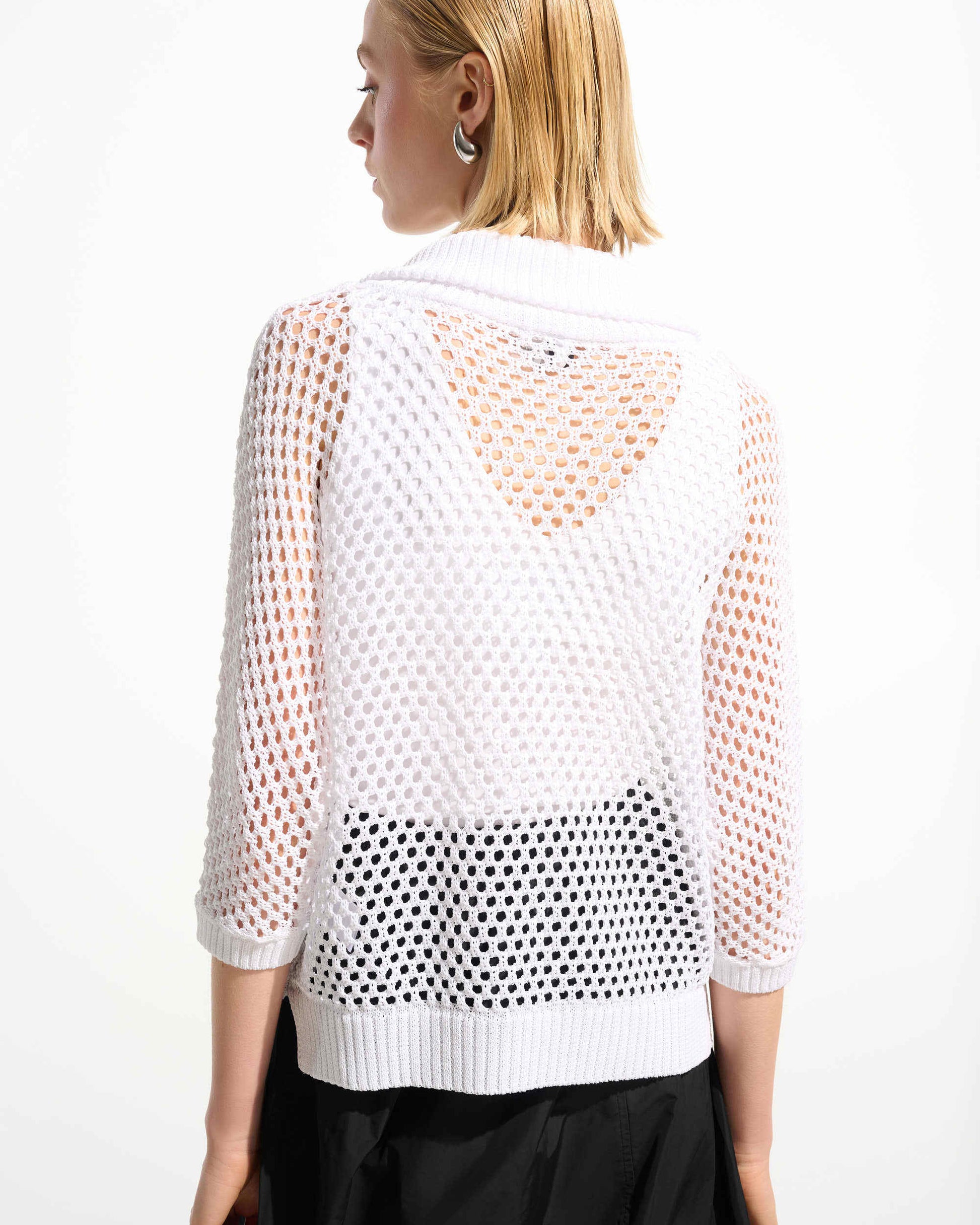 Woman wearing a white mesh top with black polka dot pattern on a plain background