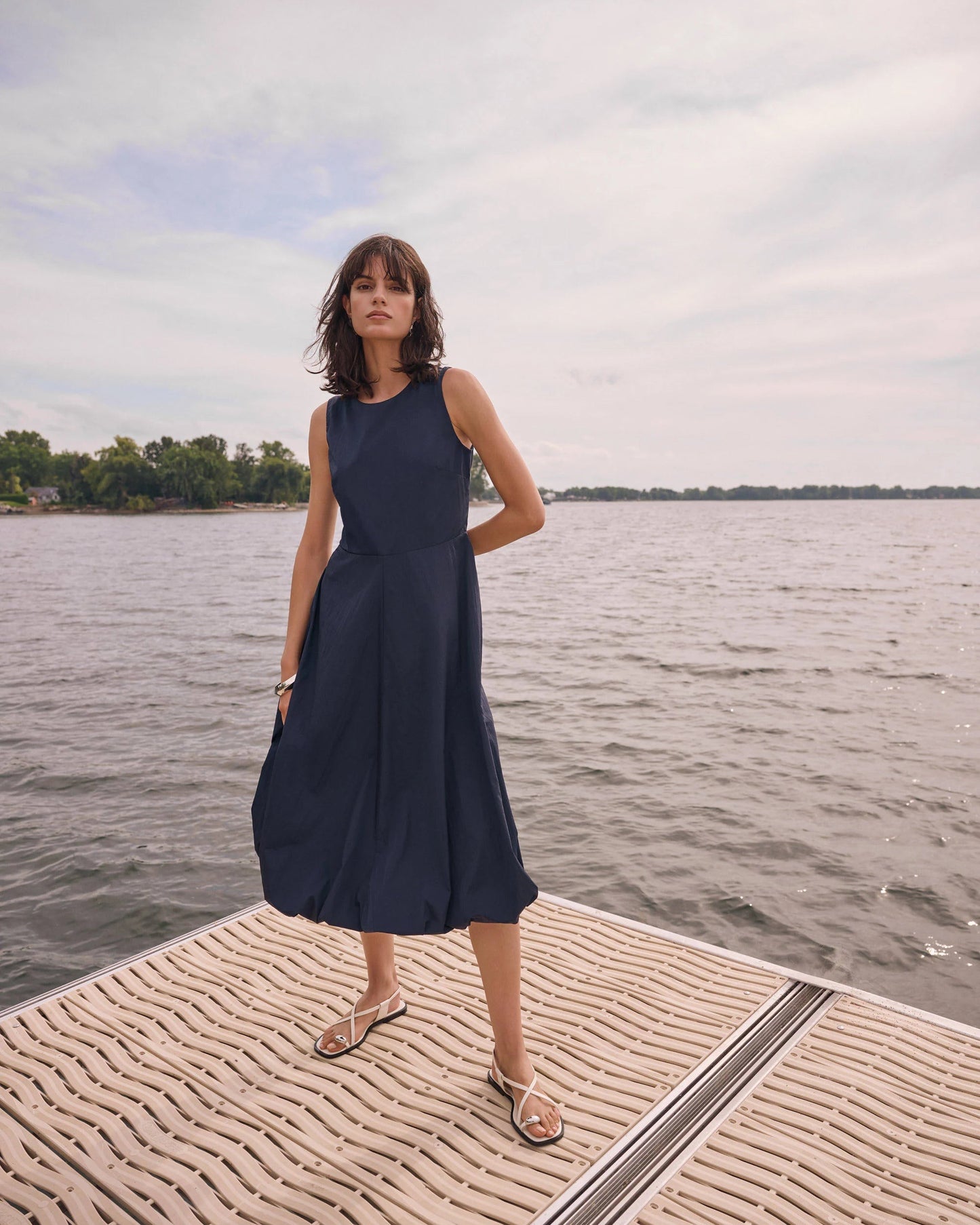 Woman in a navy dress standing on a dock by a body of water.