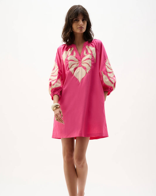 Woman wearing a pink dress with a white floral pattern on a white background