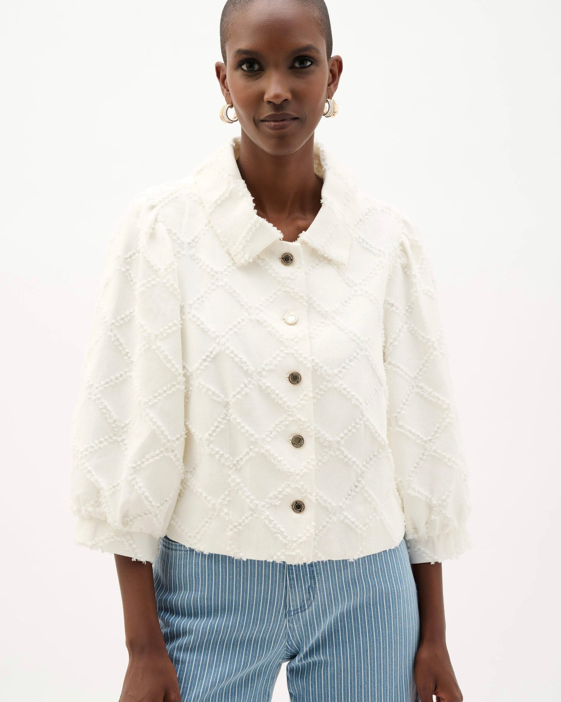 Woman wearing a white textured jacket with brown buttons on a white background