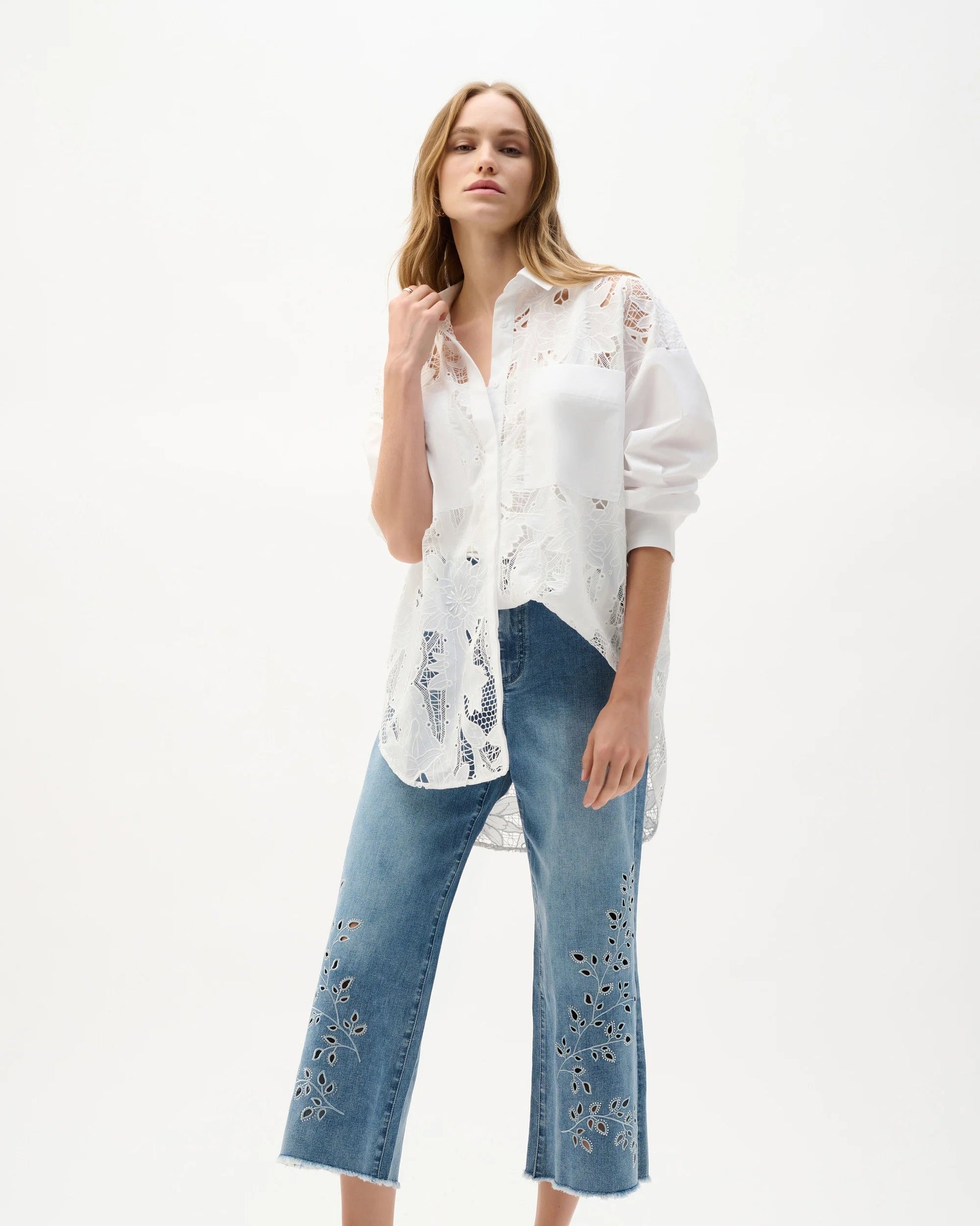 Woman wearing a white blouse with floral patterns and blue jeans on a white background