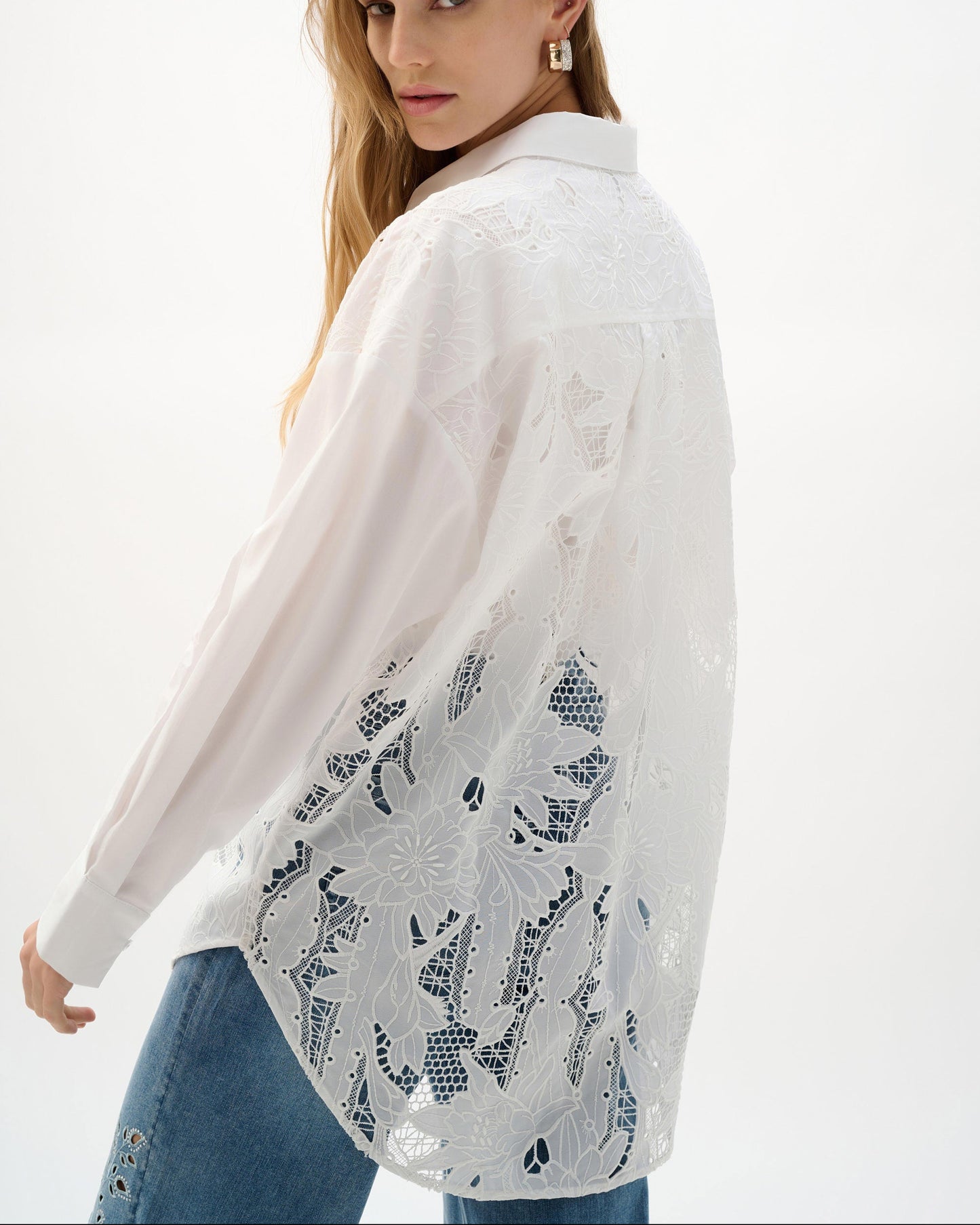 Woman wearing a white lace top over a plain shirt on a white background