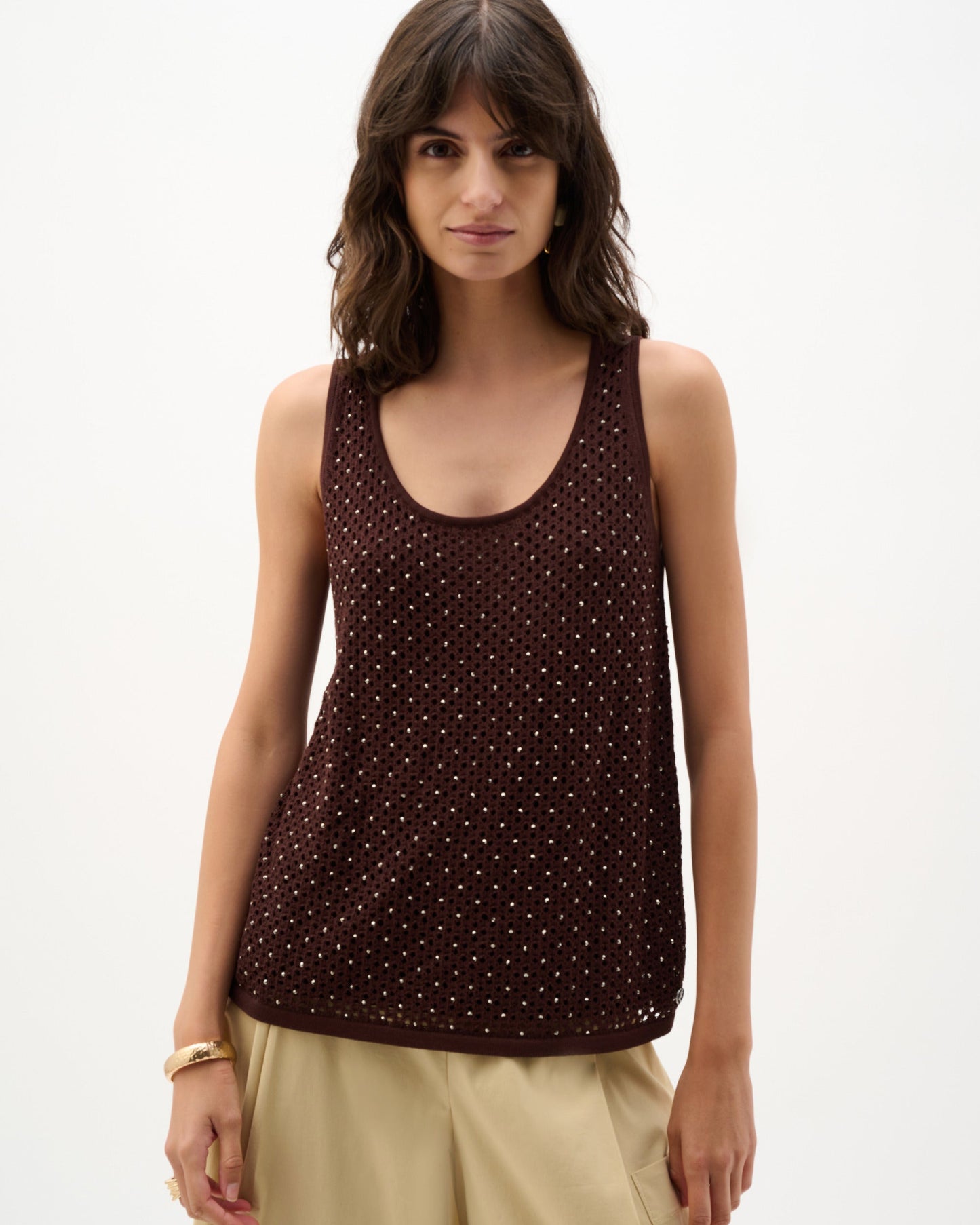 Woman wearing a brown polka dot tank top and beige pants on a white background
